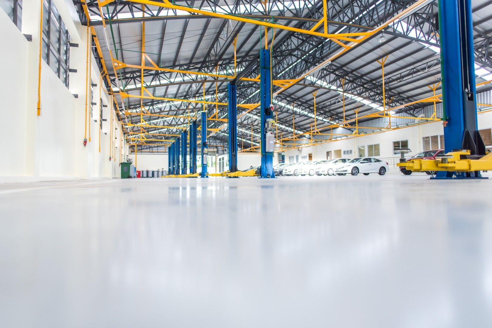 Bright, empty auto repair shop. Blue car lifts and white cars on shiny white floor.