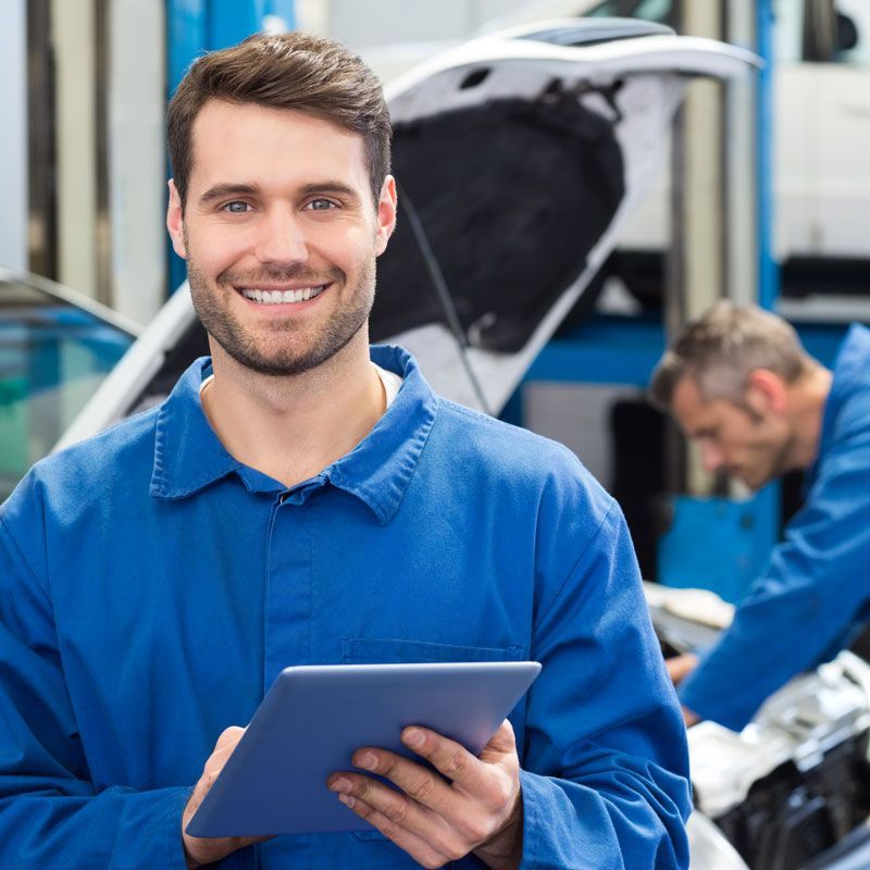 A man in a blue shirt is holding a tablet in a garage. | Brutus Auto