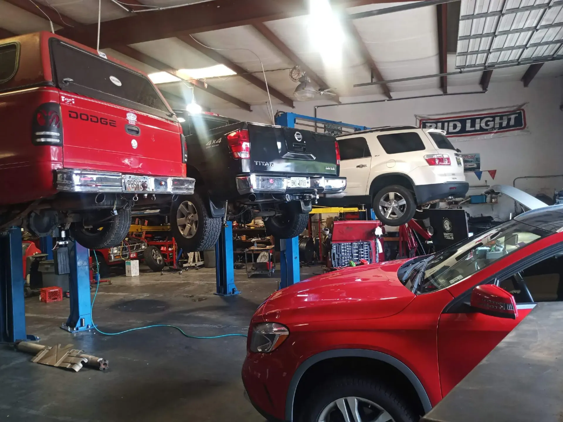 Cars on lifts inside a garage. Red, white, and black vehicles are being worked on.