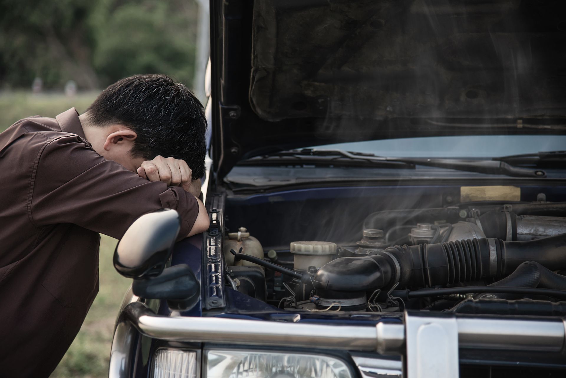Man with head on car hood; engine steaming.