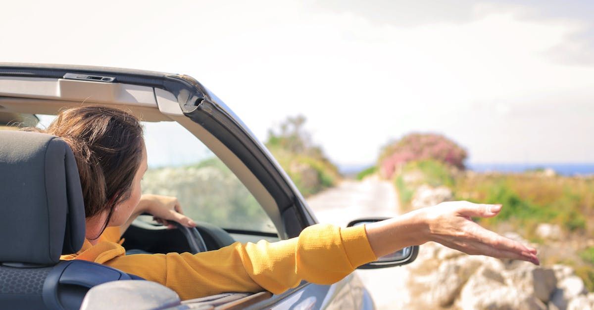 A woman is driving a convertible car down a country road.