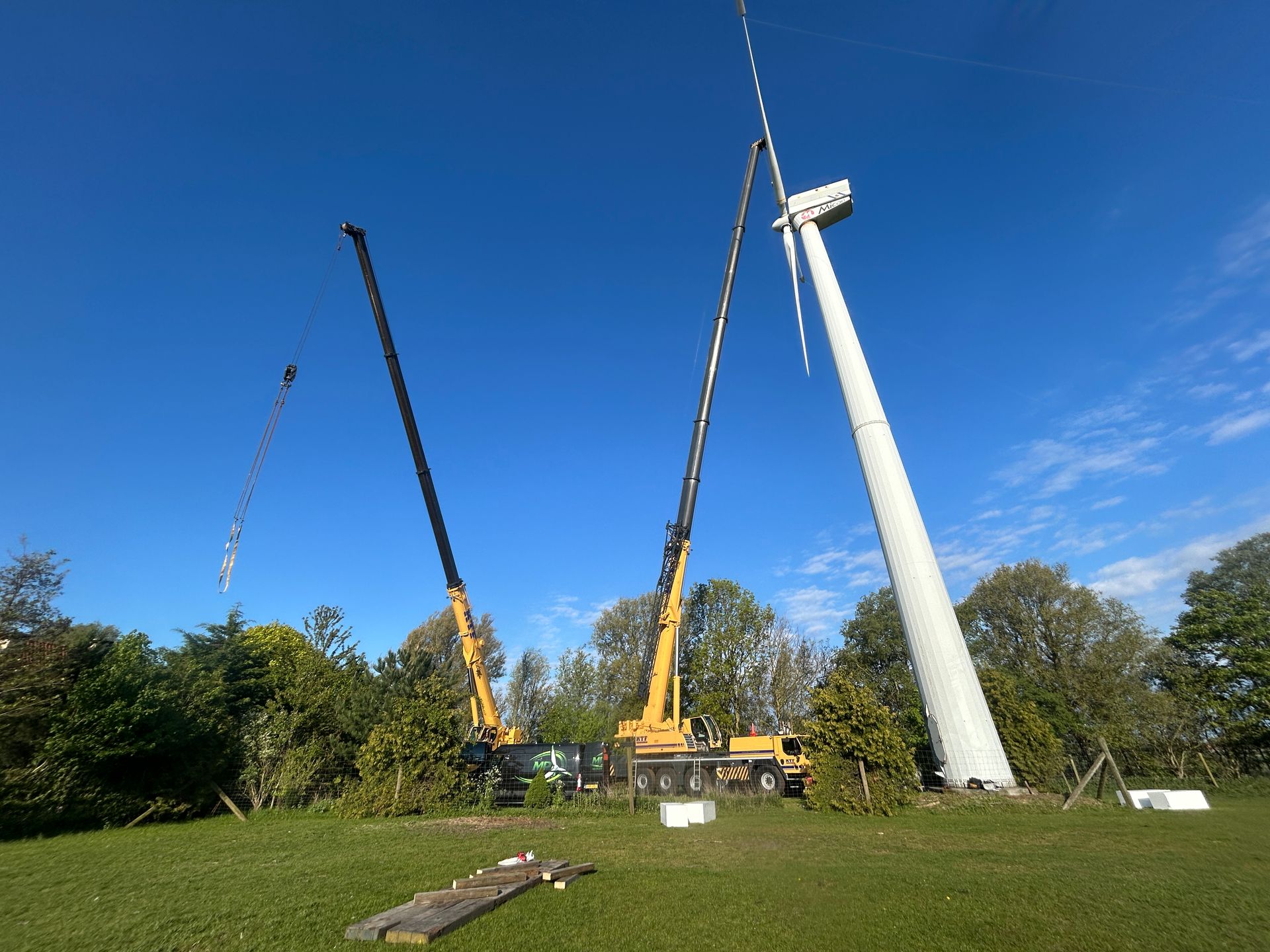 Two tall yellow cranes beside a leaning white pole in a grassy field under a blue sky