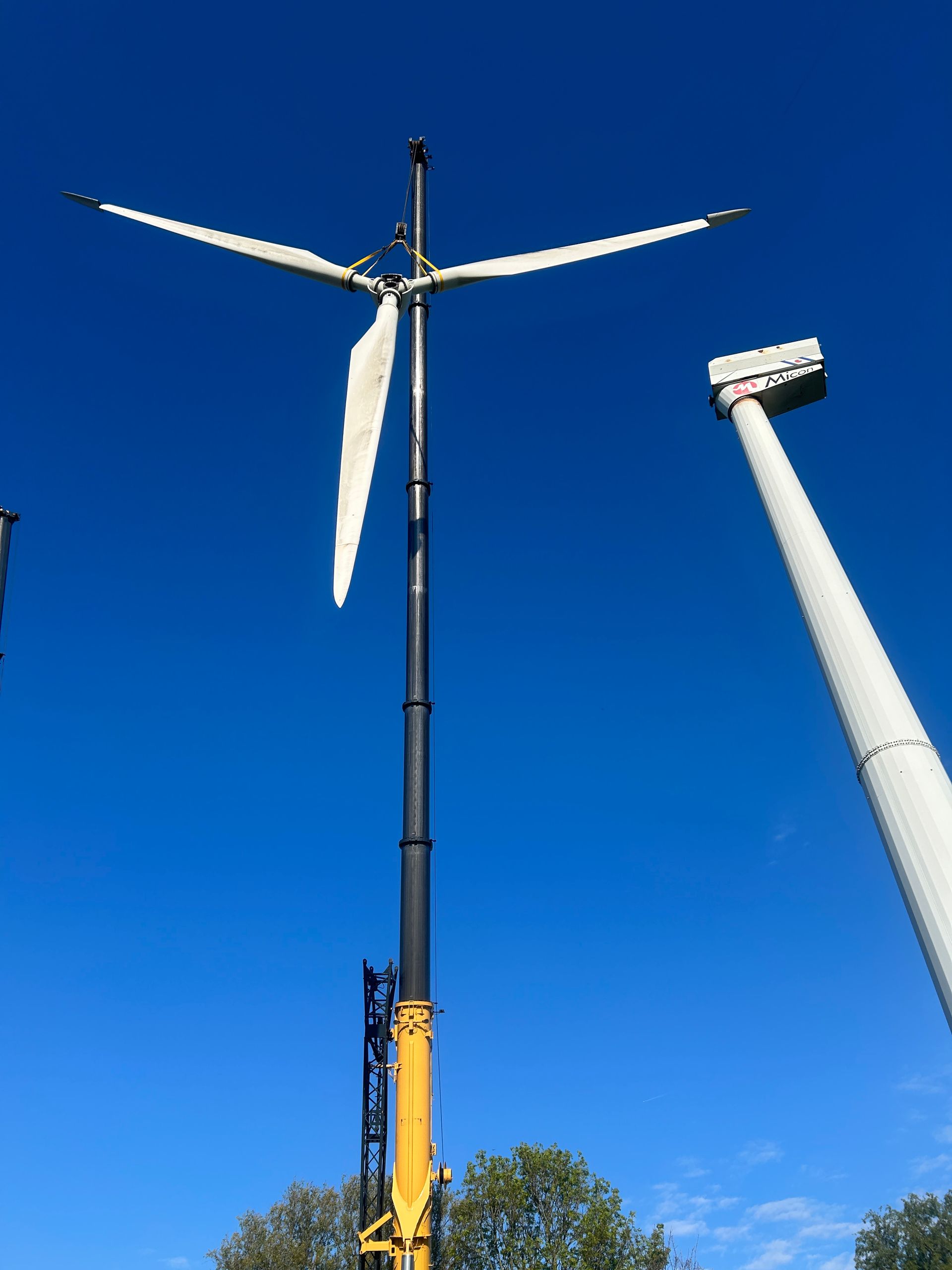 Tall wind turbine being installed by a crane against a bright blue sky