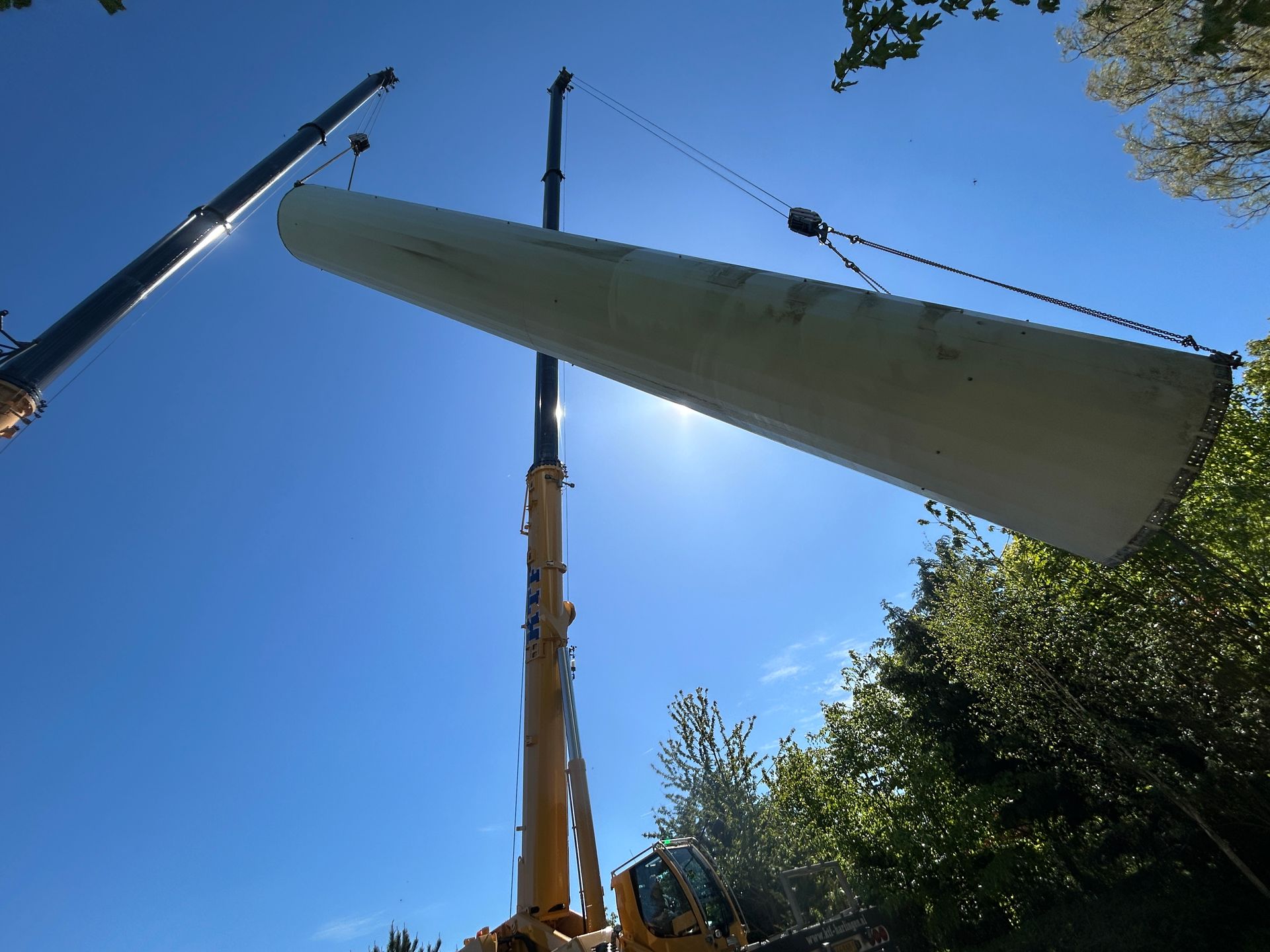 Crane lifting a large white wind turbine blade against a bright blue sky