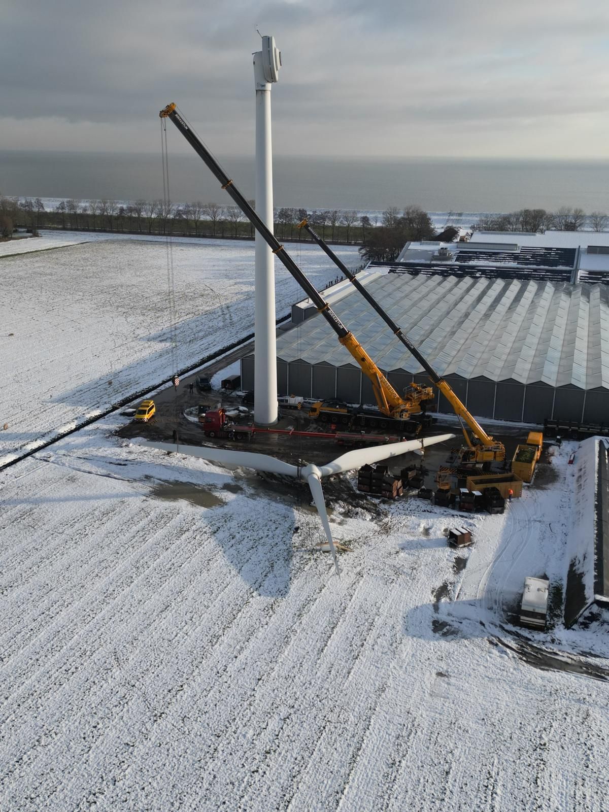 Construction equipment on a snowy rooftop beside a tall white chimney stack