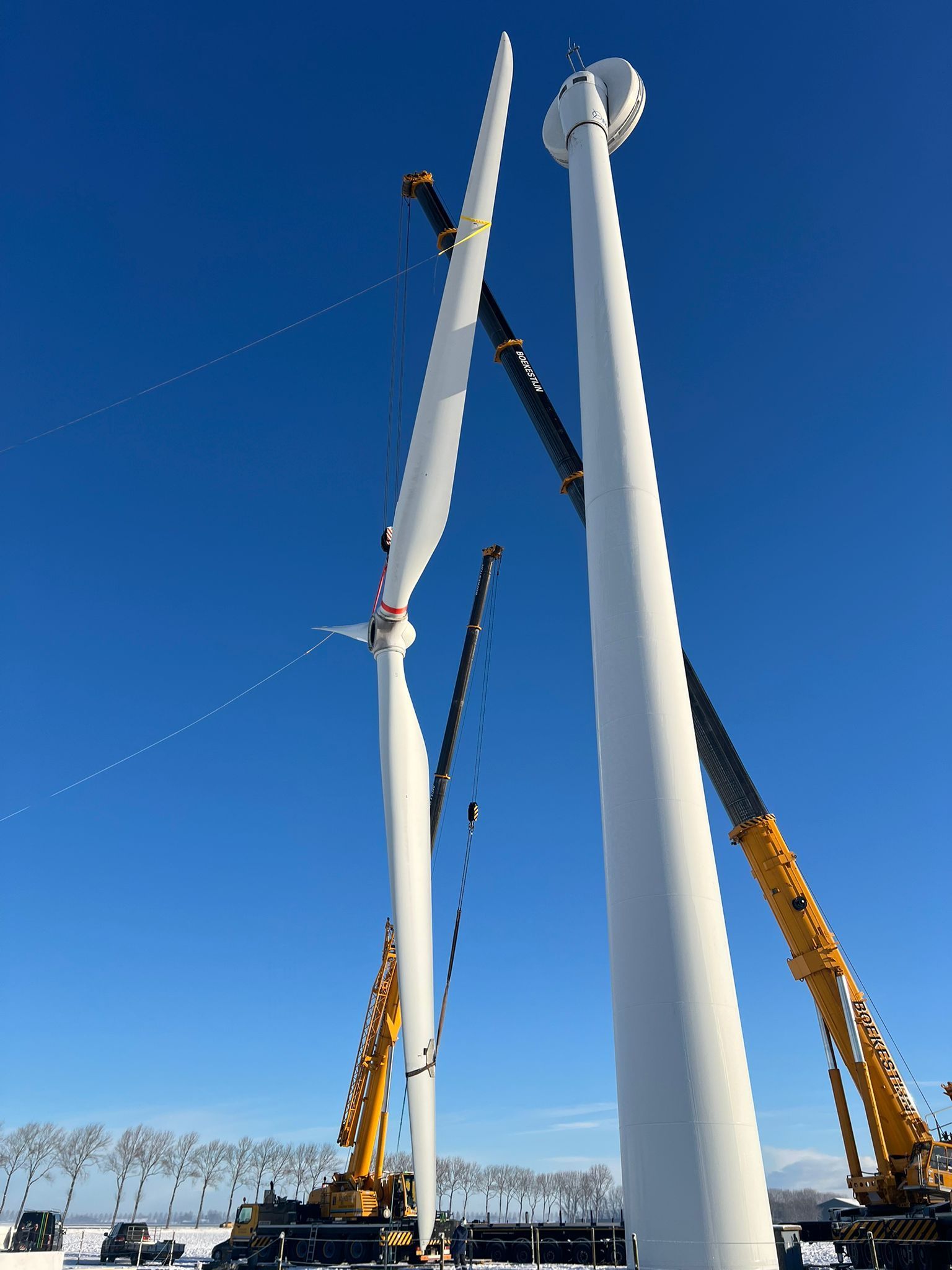 Two white wind turbine towers being installed by cranes against a clear blue sky