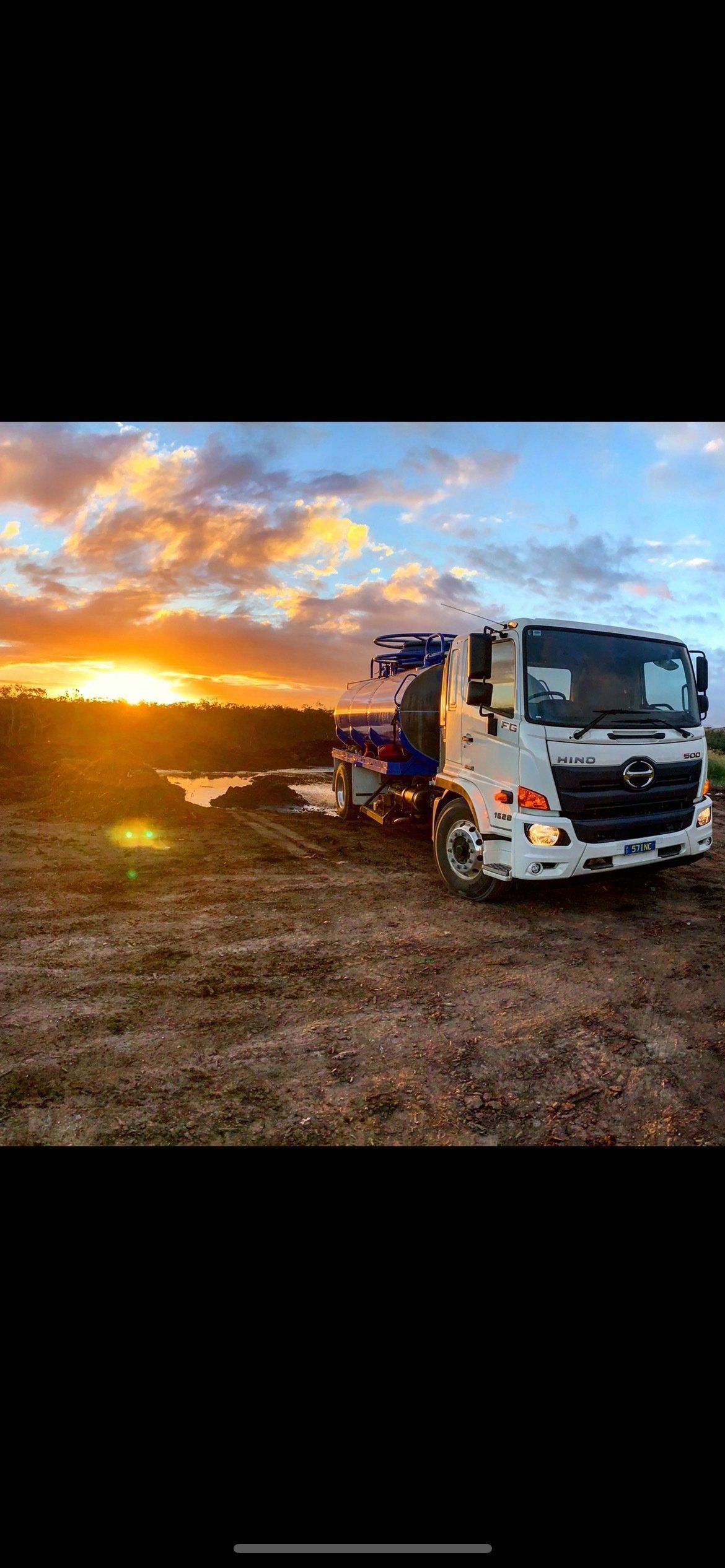 A truck is parked in a field at sunset.