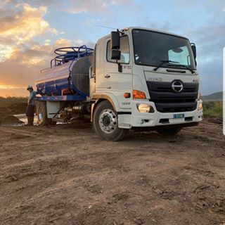 A white truck with a blue tank is parked in a dirt field.
