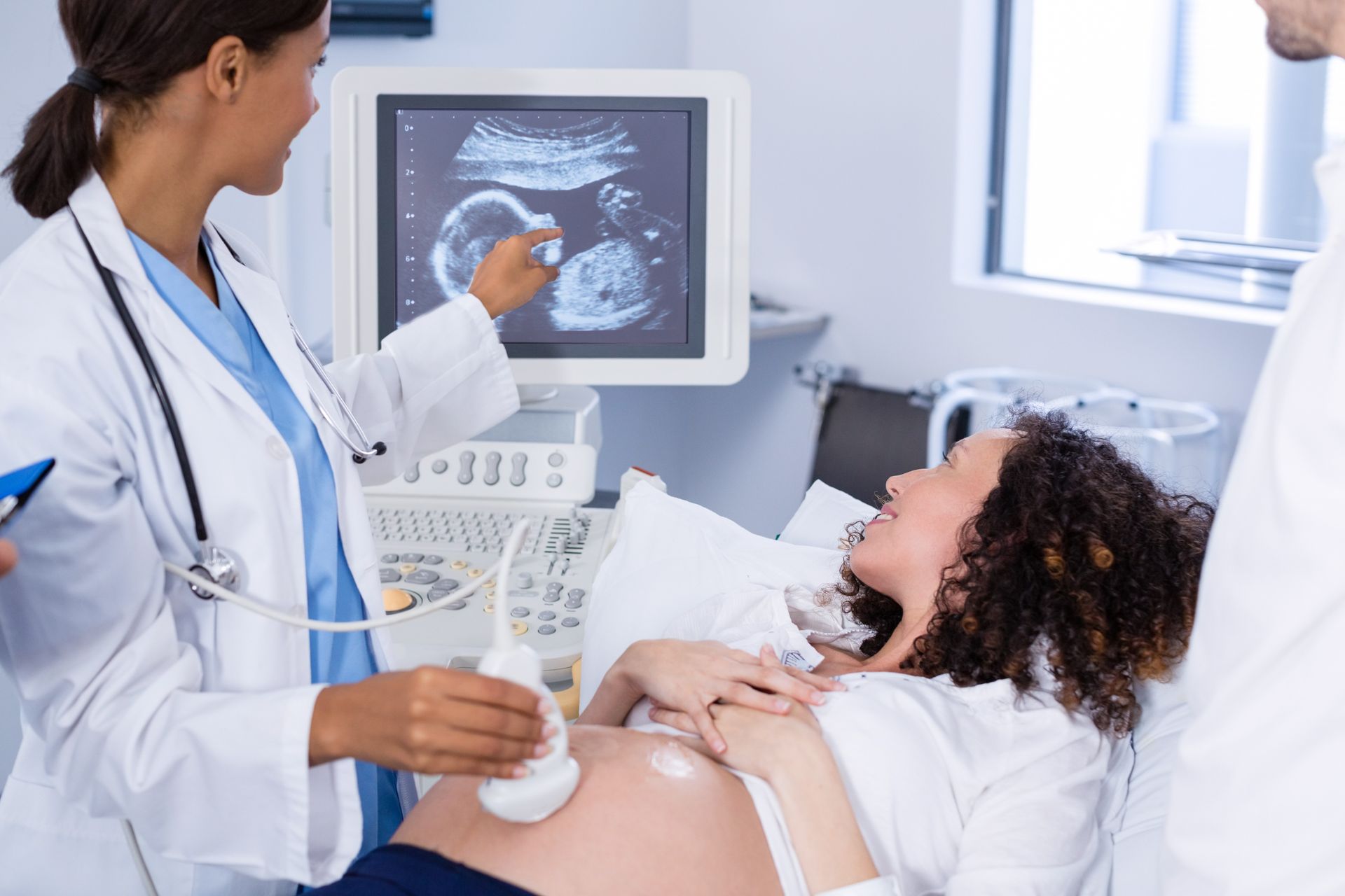 A doctor in a white coat performing an ultrasound on a pregnant patient in a clinic.
