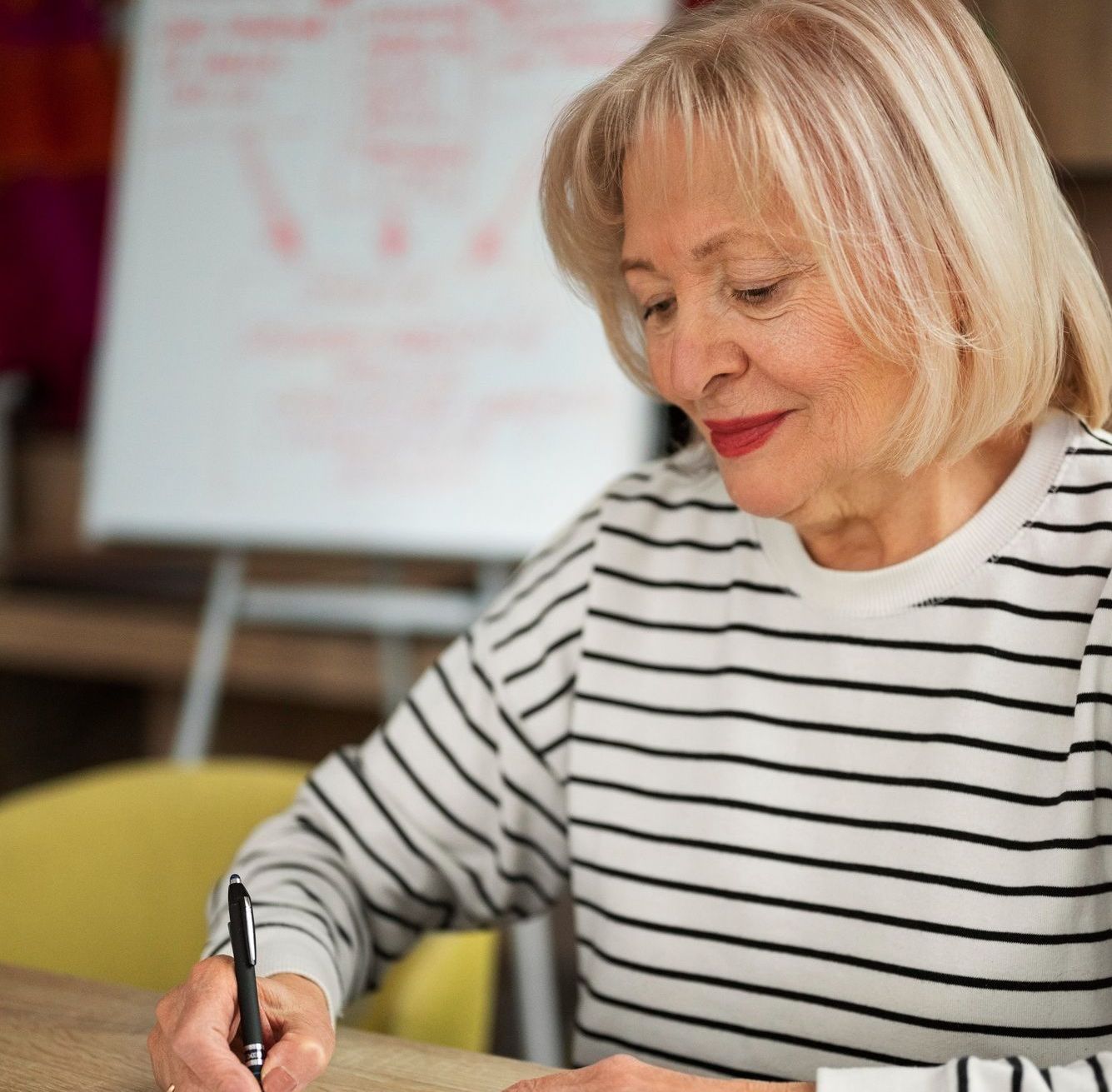 A woman in a striped shirt is writing on a piece of paper