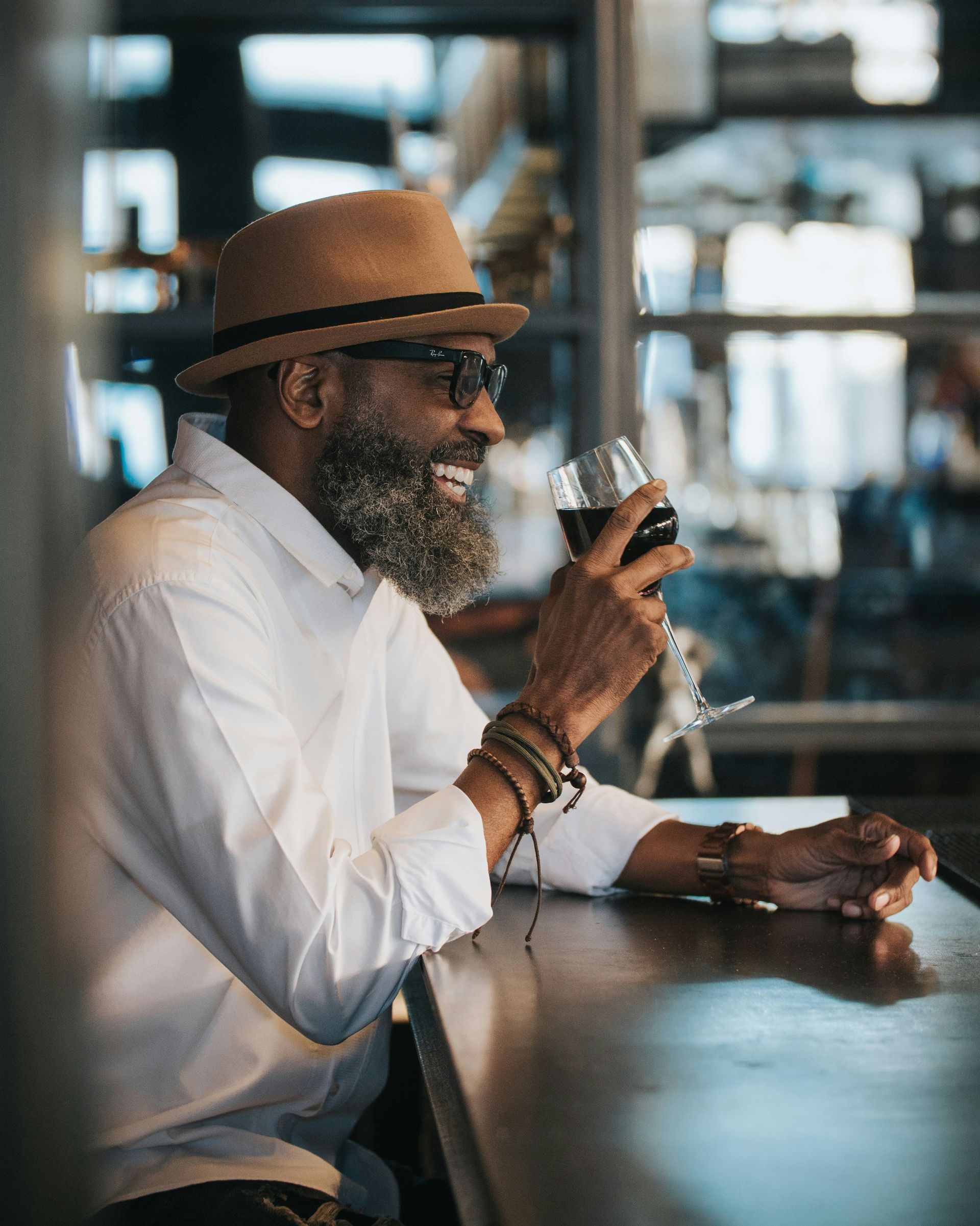 A man with a beard is sitting at a bar holding a glass of wine.