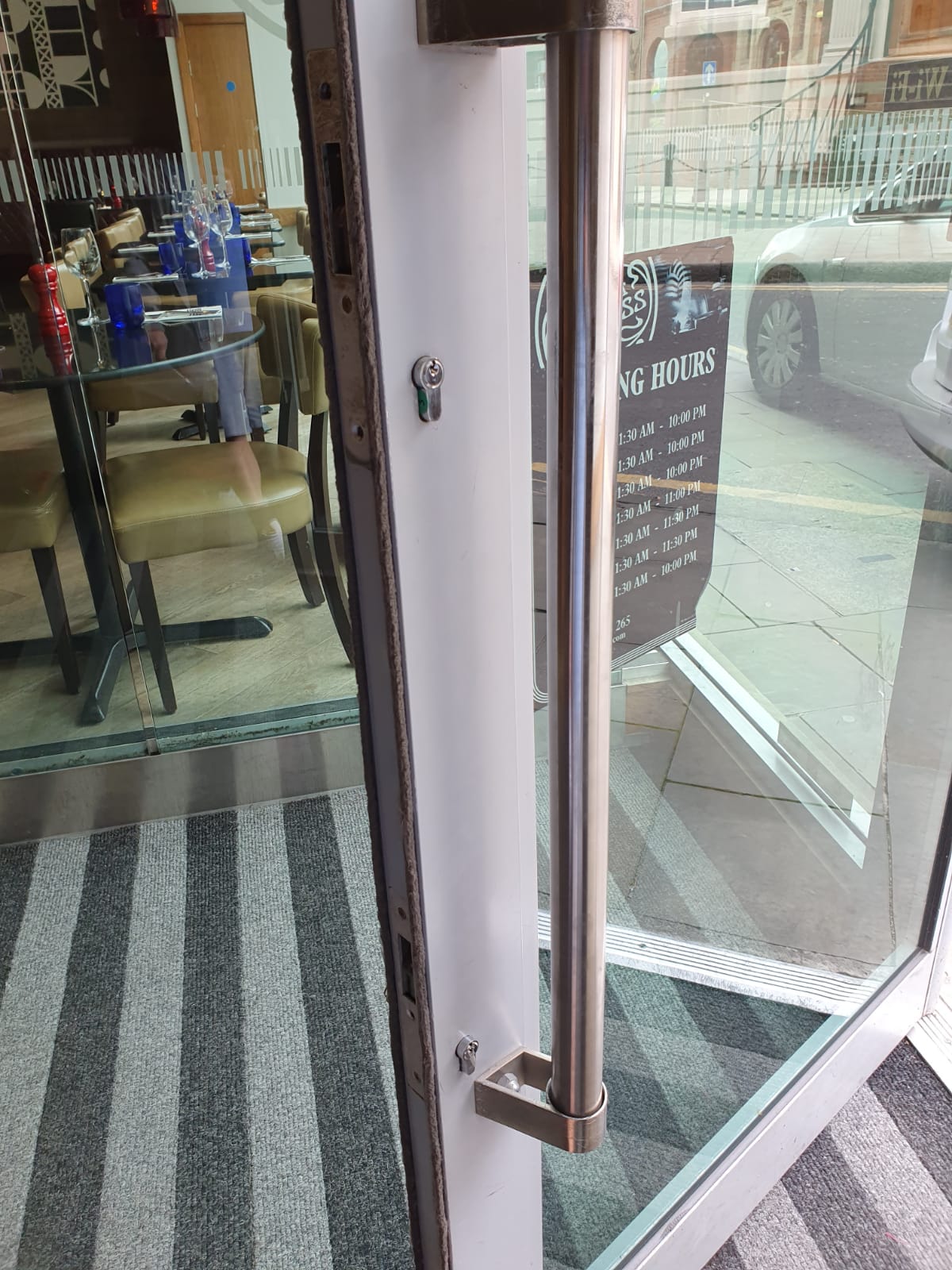 A glass door with a stainless steel handle is open to a restaurant.