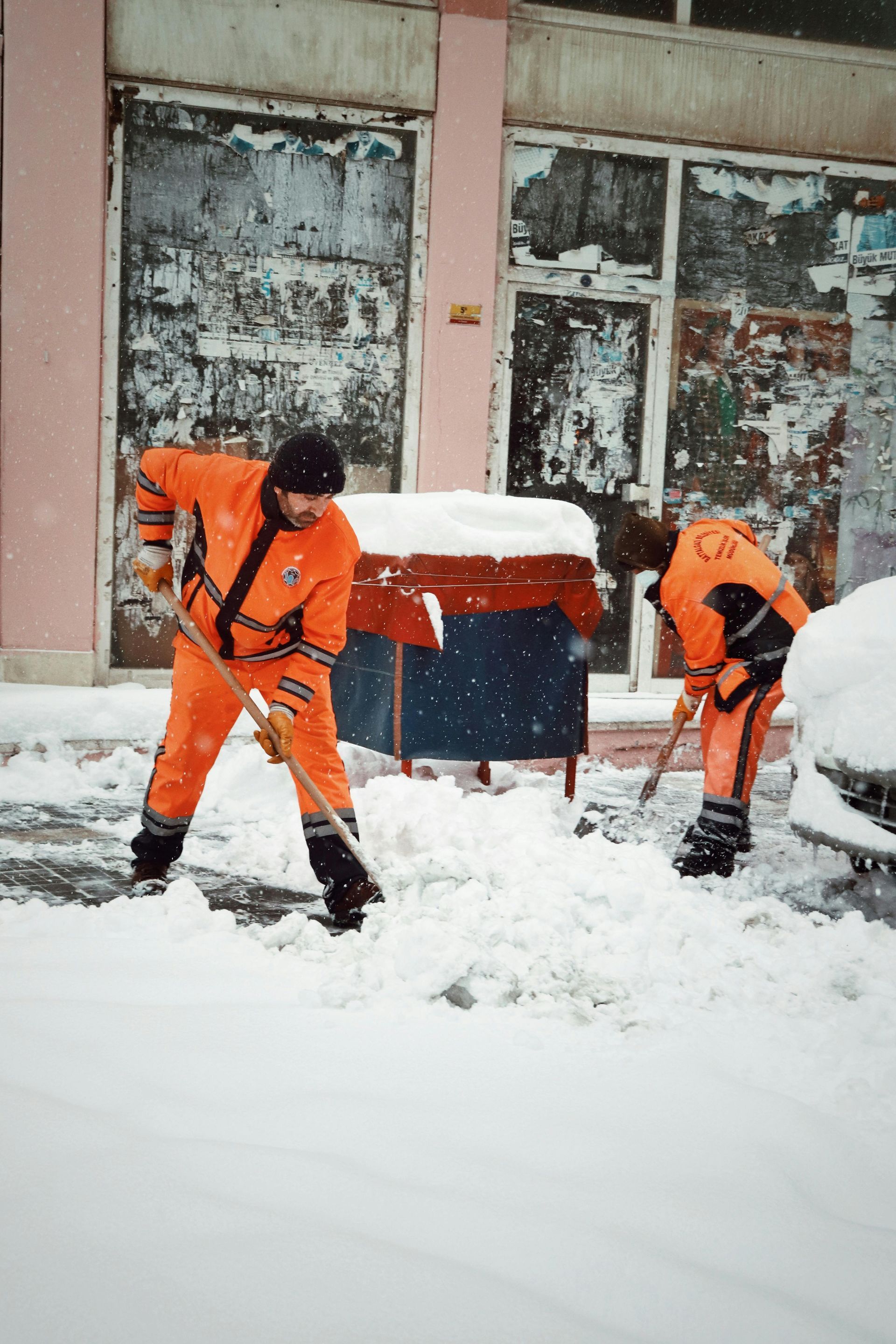 Two men are shoveling snow in front of a building