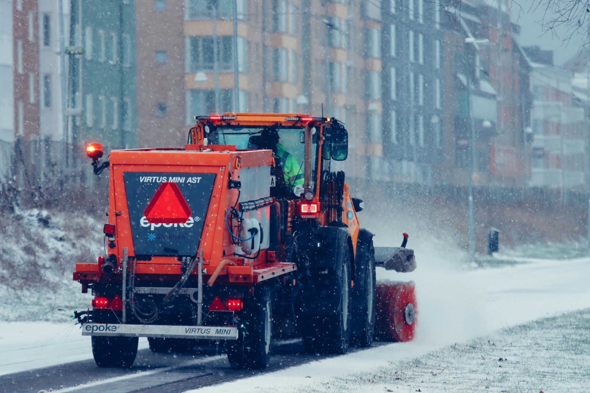 A tractor is driving down a snow covered road.