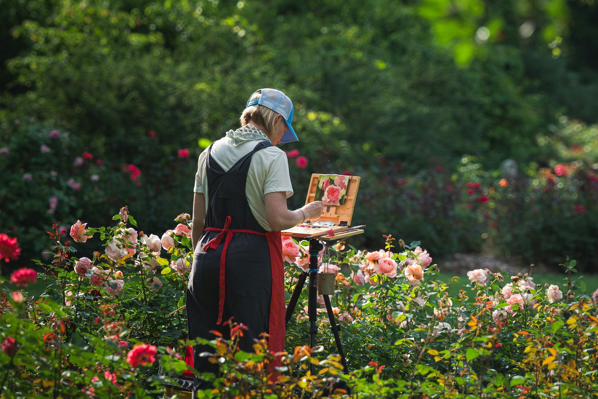A woman is painting a picture of roses in a garden.
