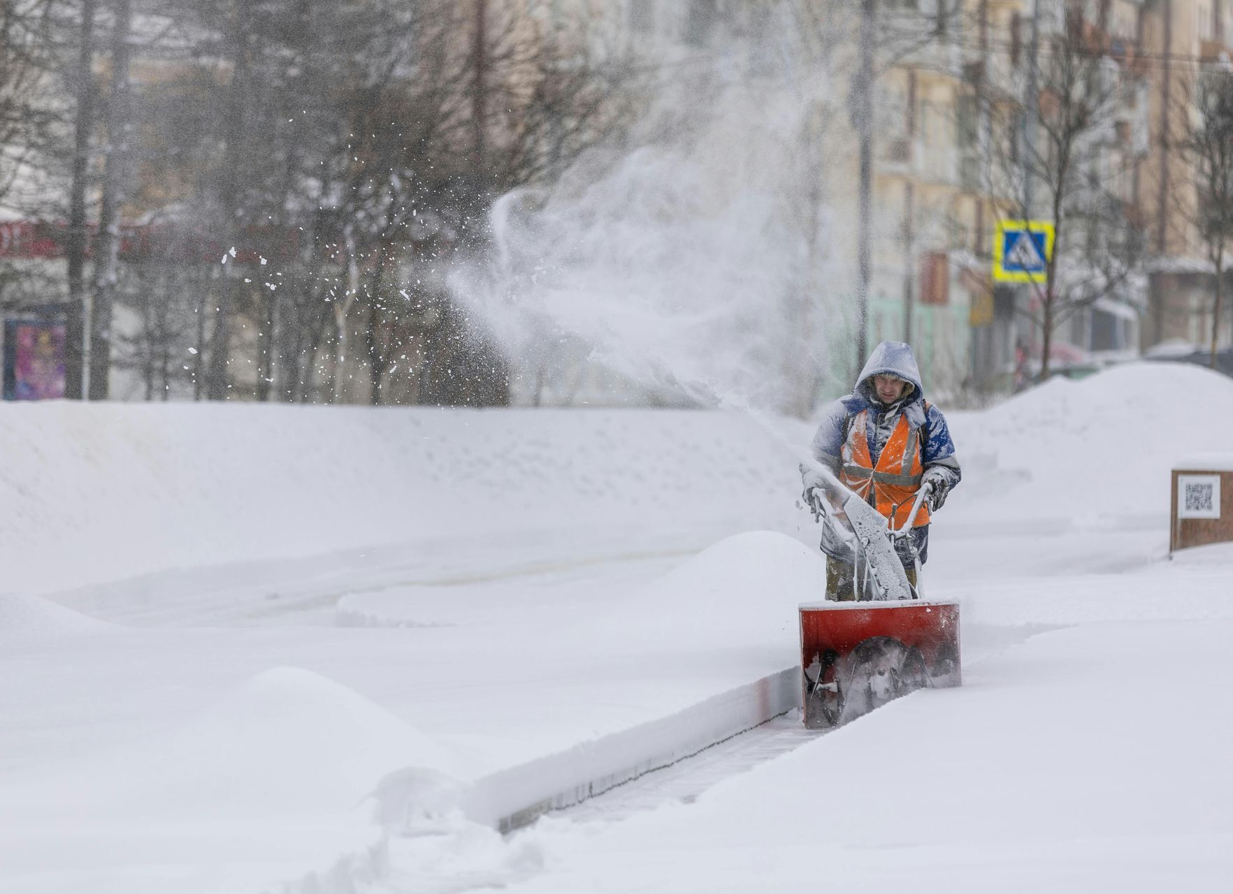 A man is using a snow blower to remove snow from the sidewalk.