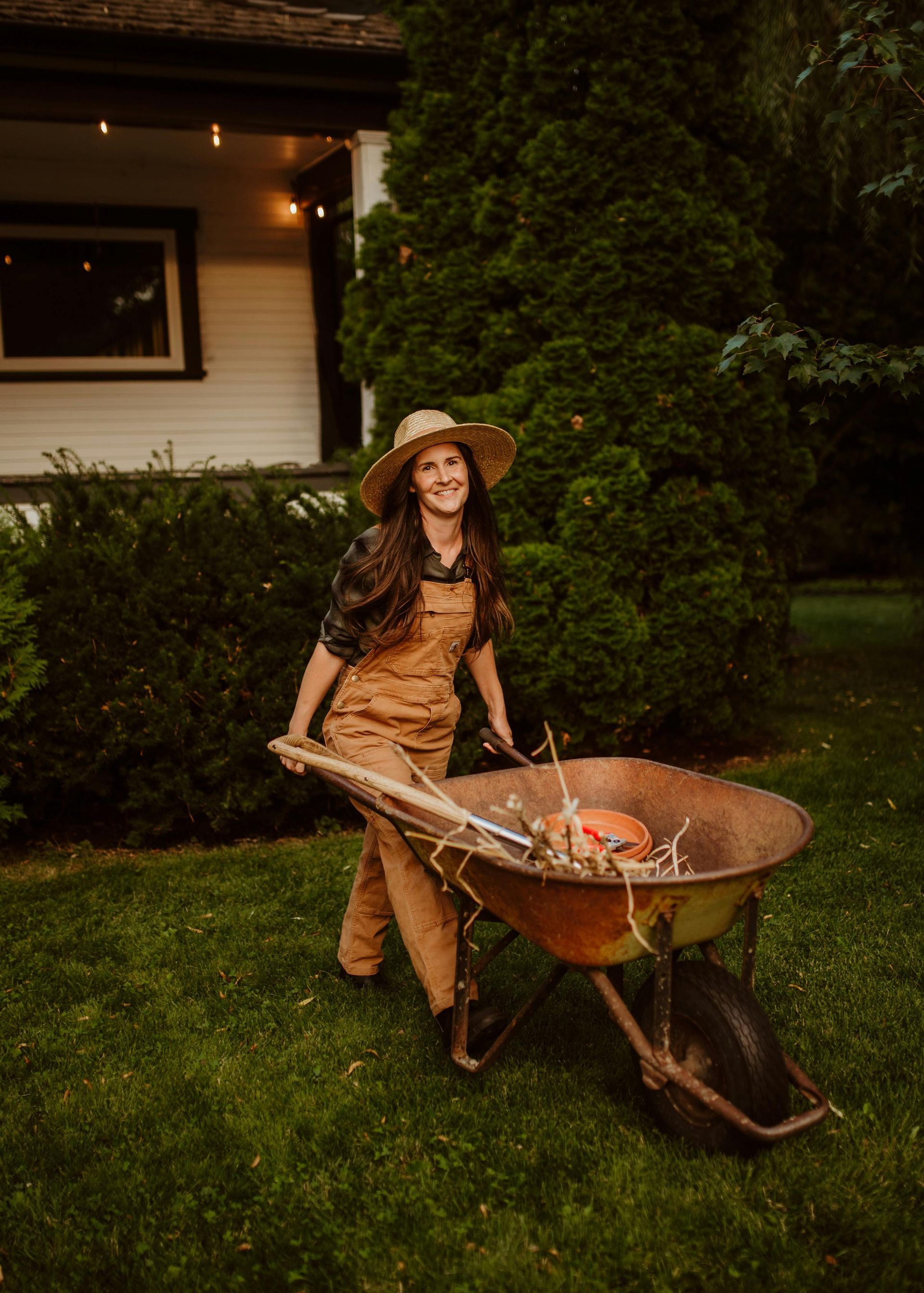 Lady pushing a wheel-barrel across her green lawn