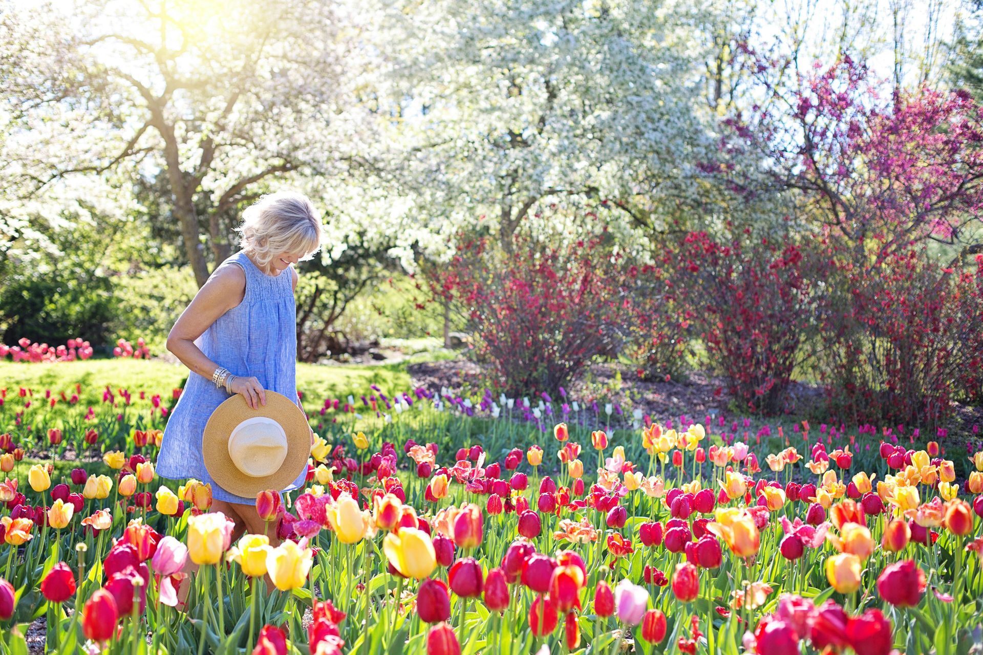 A woman in a blue dress and hat is standing in a field of flowers.