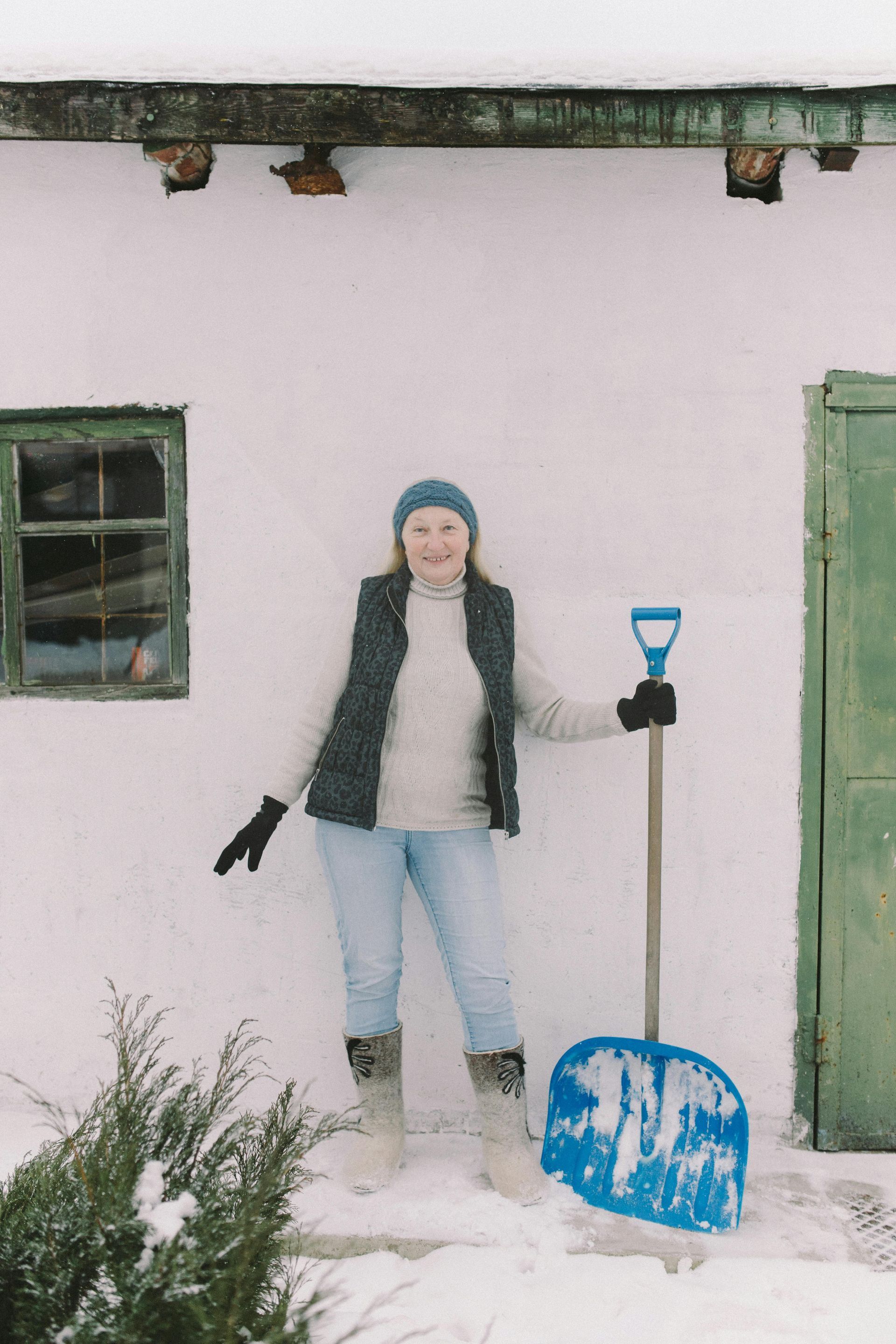 A woman is standing in the snow holding a snow shovel.