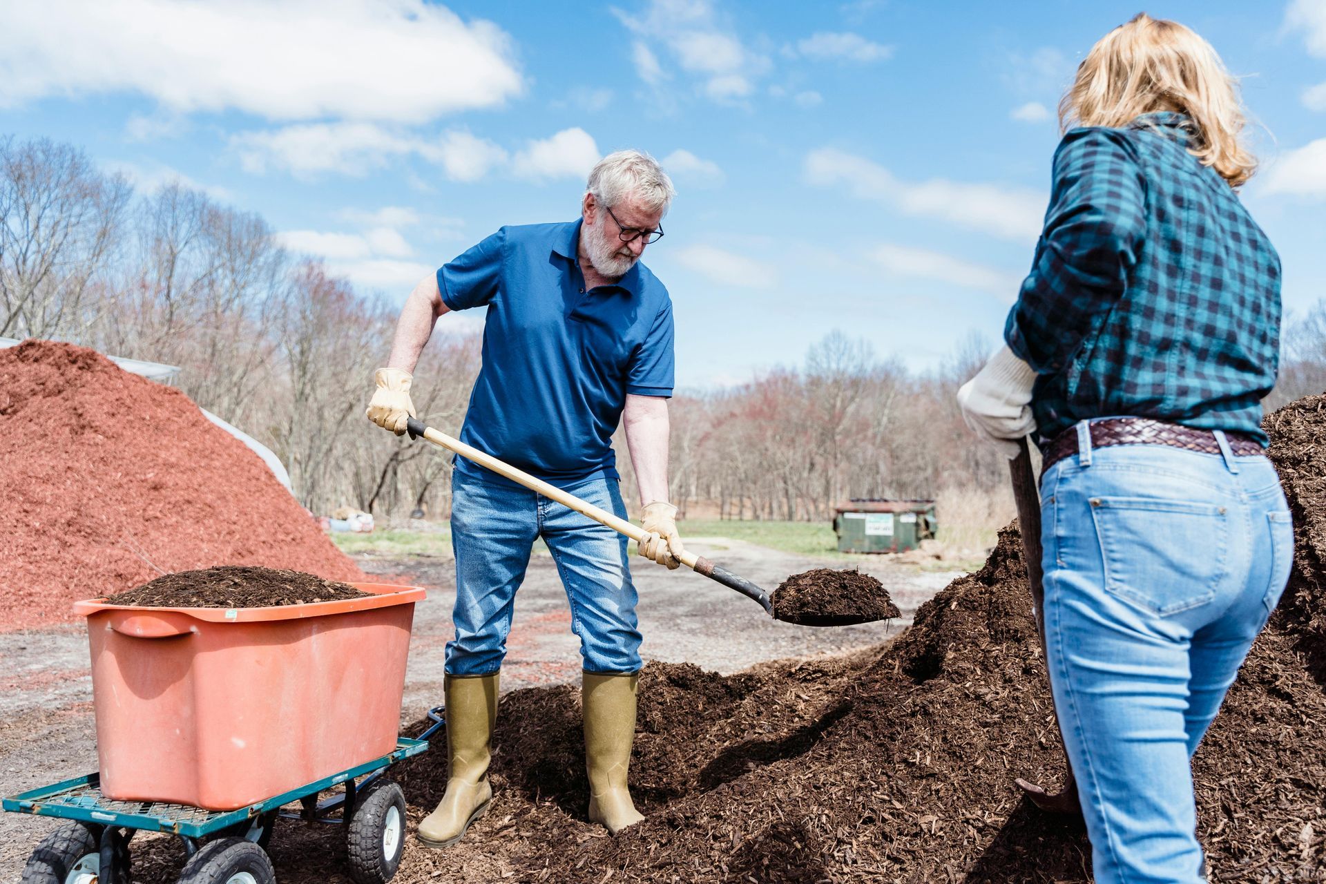 A man is shoveling dirt into a cart while a woman looks on.