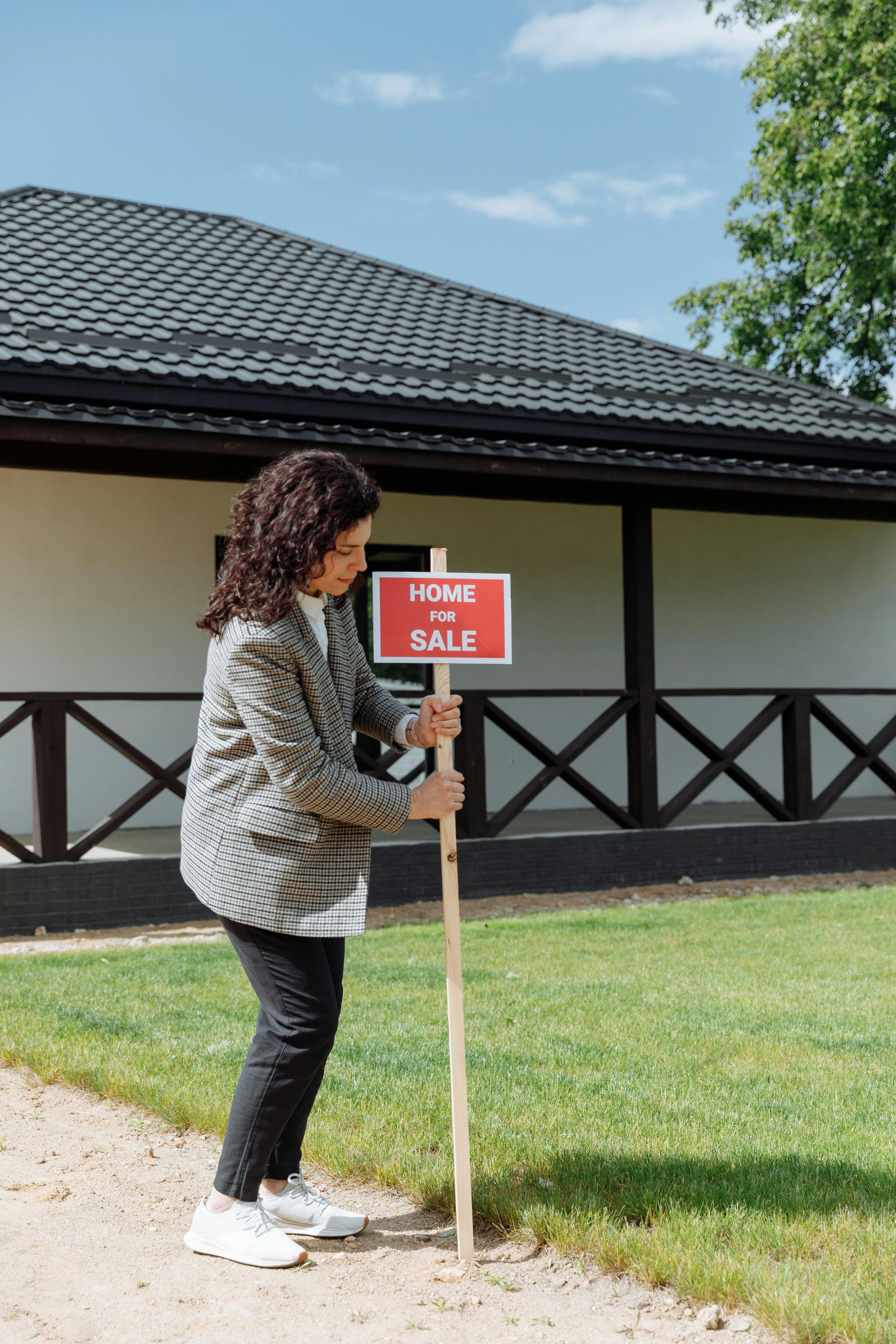 A woman is holding a for sale sign in front of a house.
