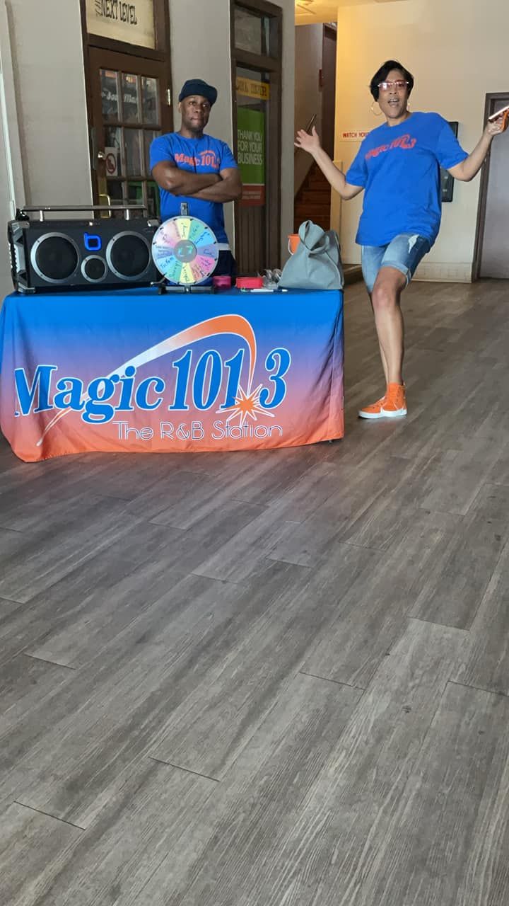 Two people at a Magic 101.3 table. One is dancing, the other stands with arms crossed.