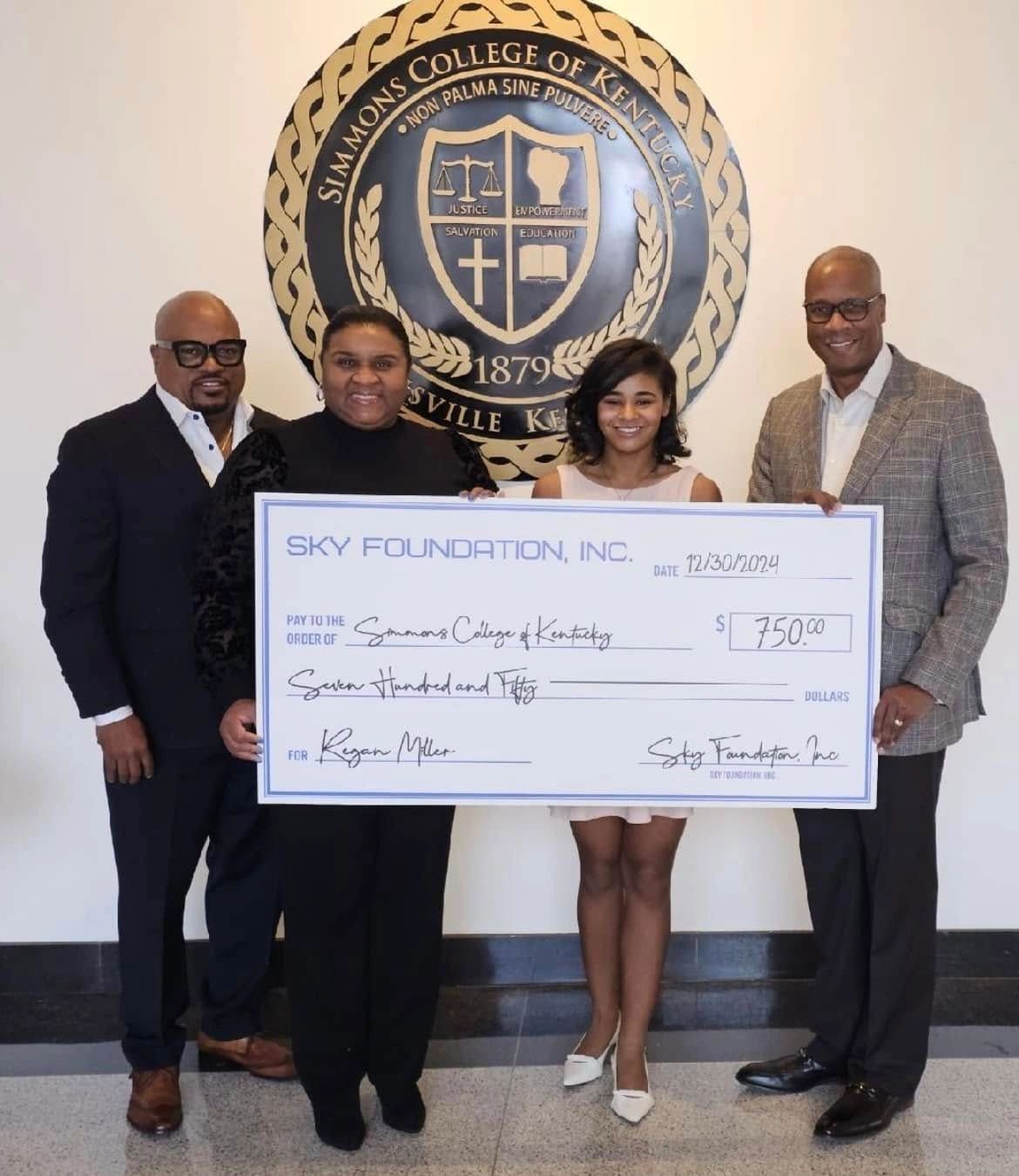 Four people posing with a large check in front of the Simmons College emblem.