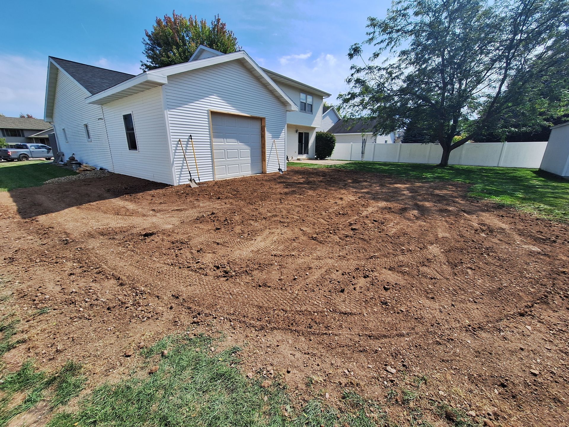 Dirt patch in a yard next to a white garage. Lawn is partially visible in the foreground.