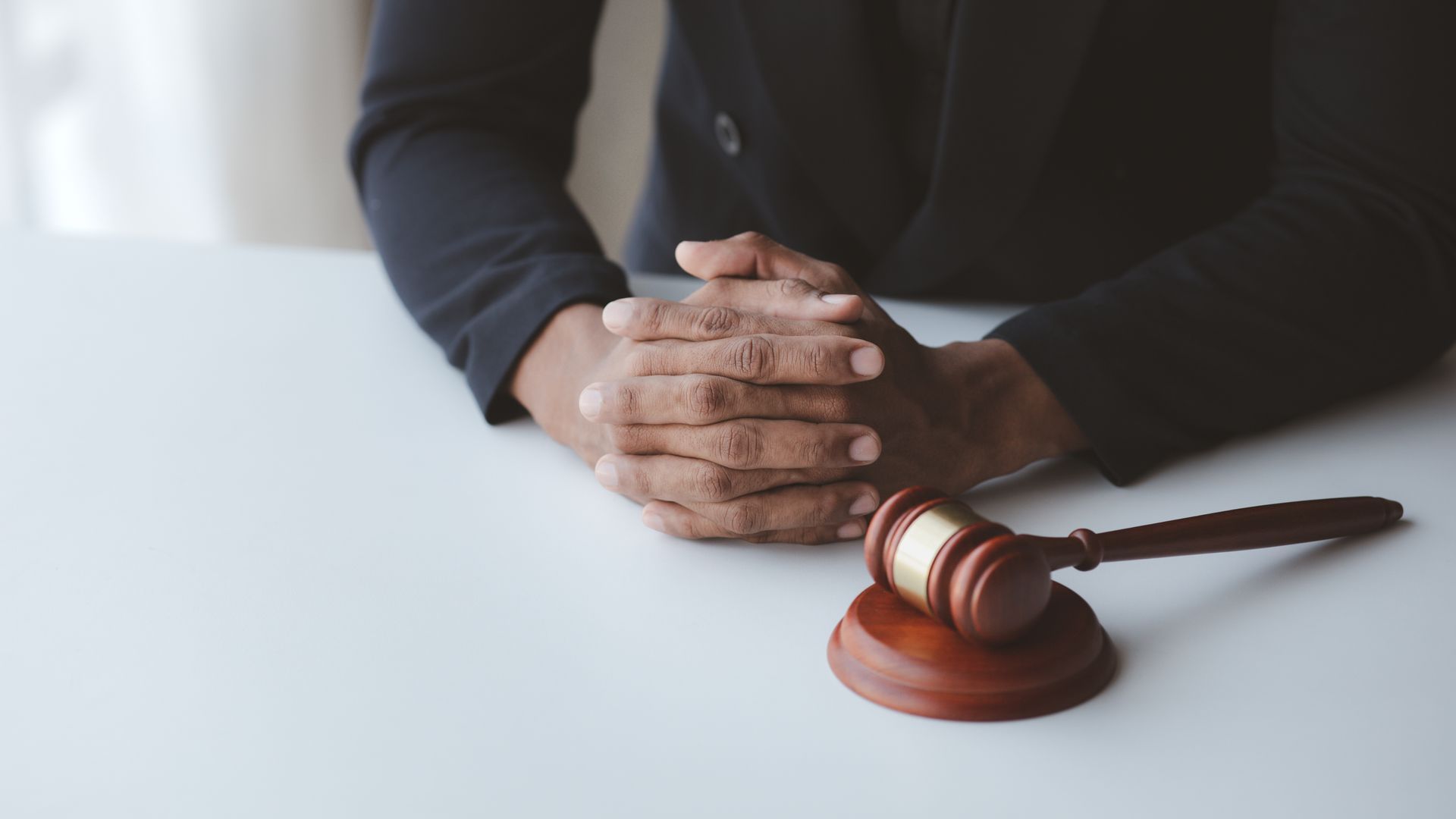 Hands clasped on white table with wooden gavel.
