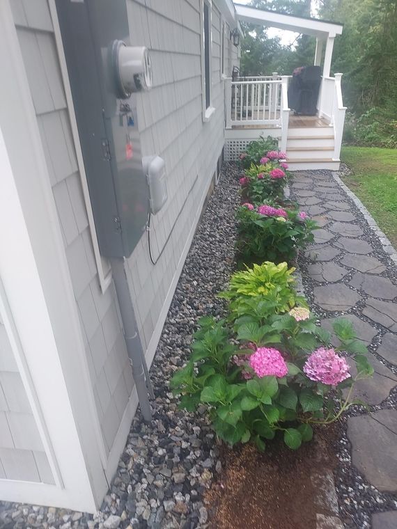 Two red Adirondack chairs under a wooden pergola on a concrete patio, against a white building.