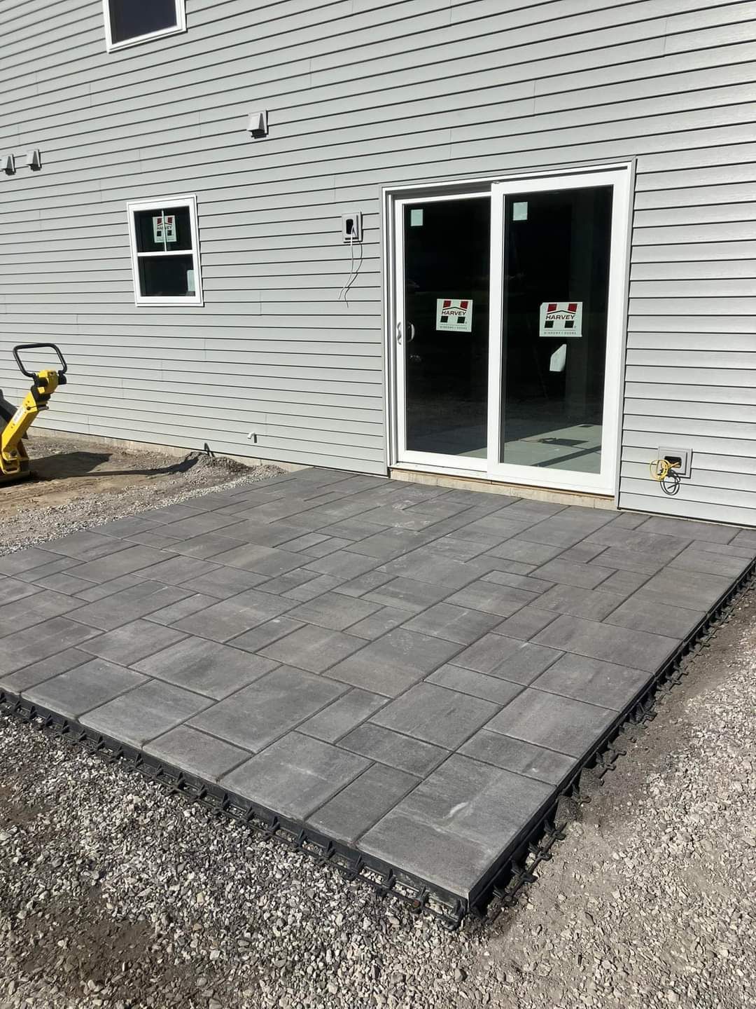 Gray brick patio outside a house with a sliding glass door; a small window is visible.