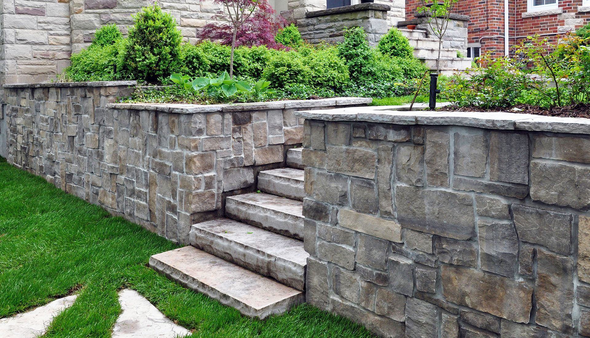 Stone retaining walls with steps leading to a garden with green plants.