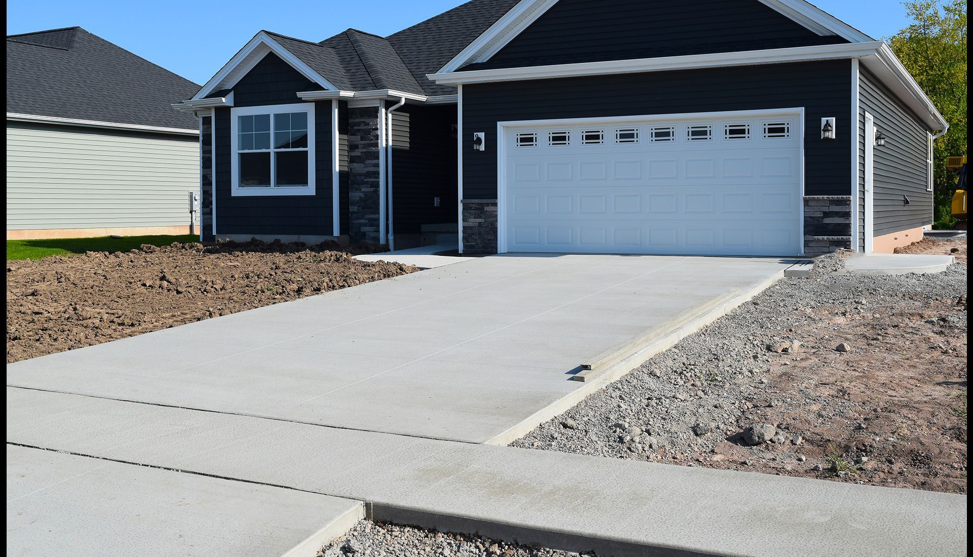 A newly built house with a gray concrete driveway and garage in a sunny setting.