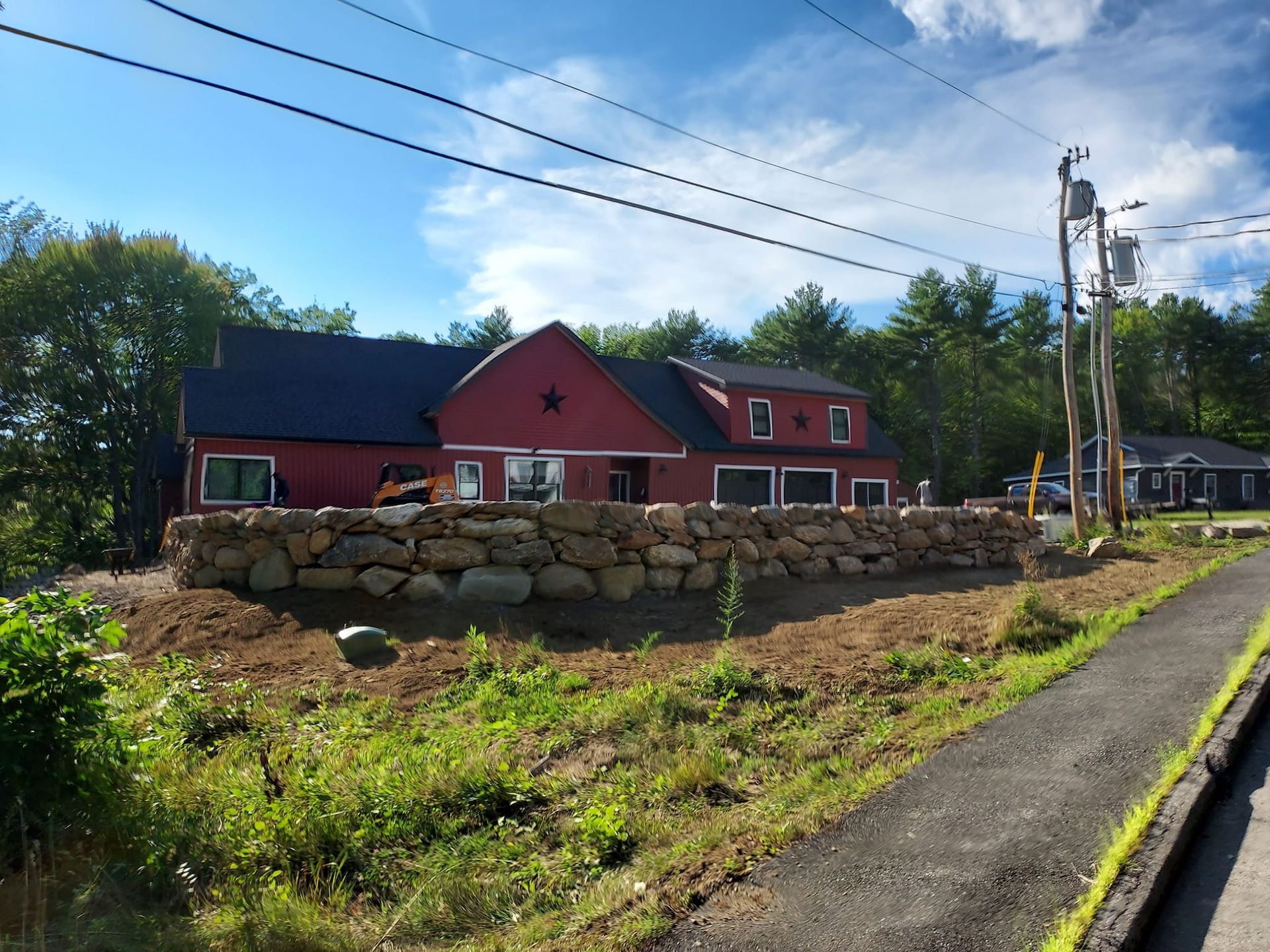 Red barn with a stone wall in front, along a road.