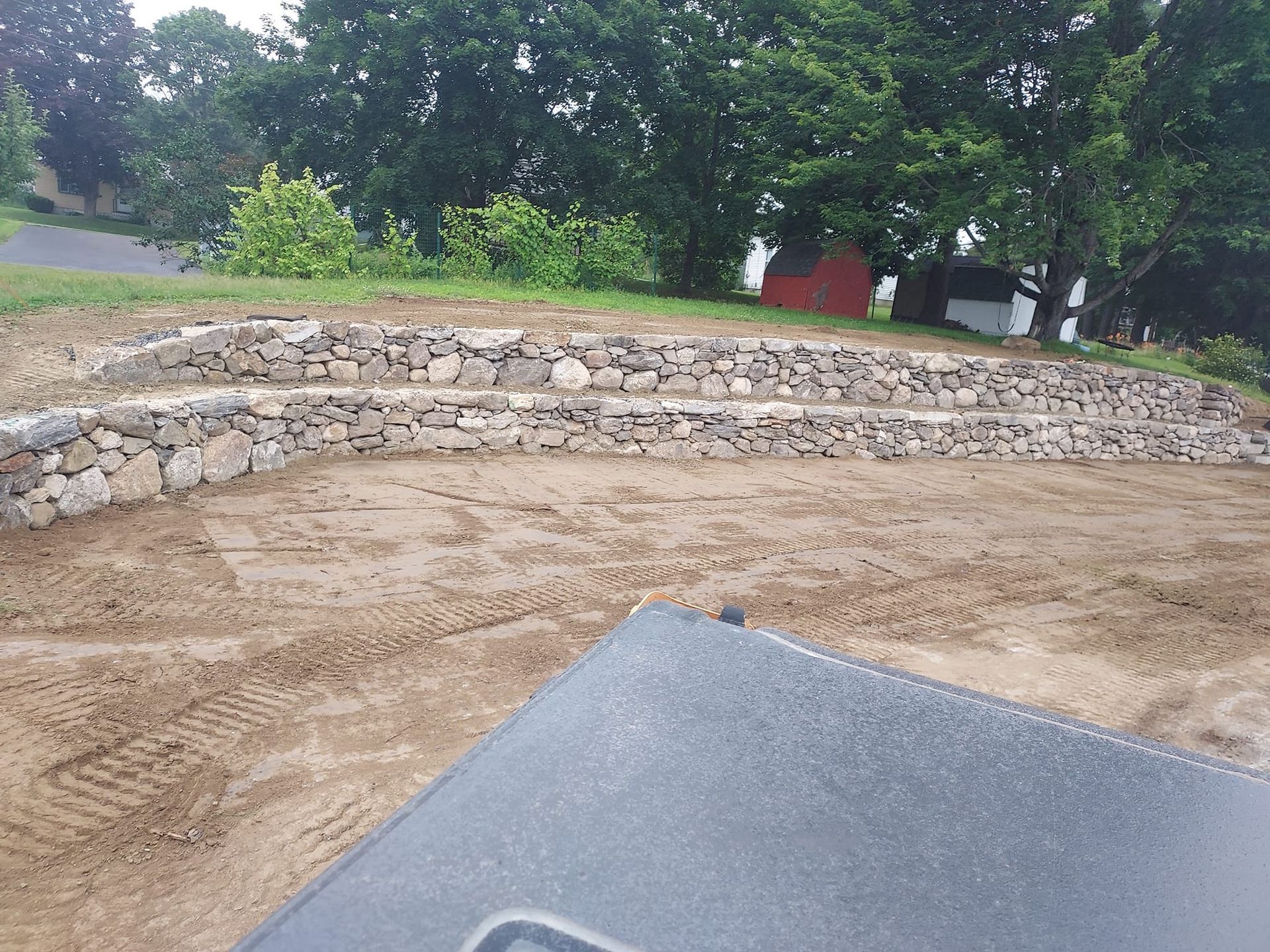 Stone retaining walls on a graded, sandy lot with trees in the background.