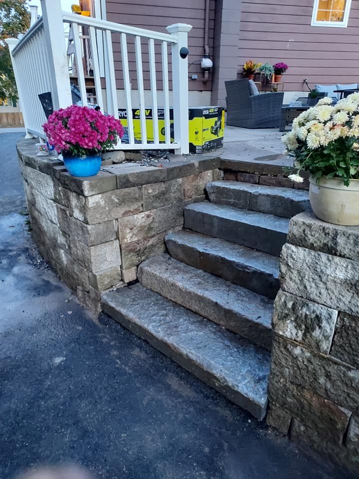 Stone steps leading up to a white railing, with potted flowers and a patio in the background.
