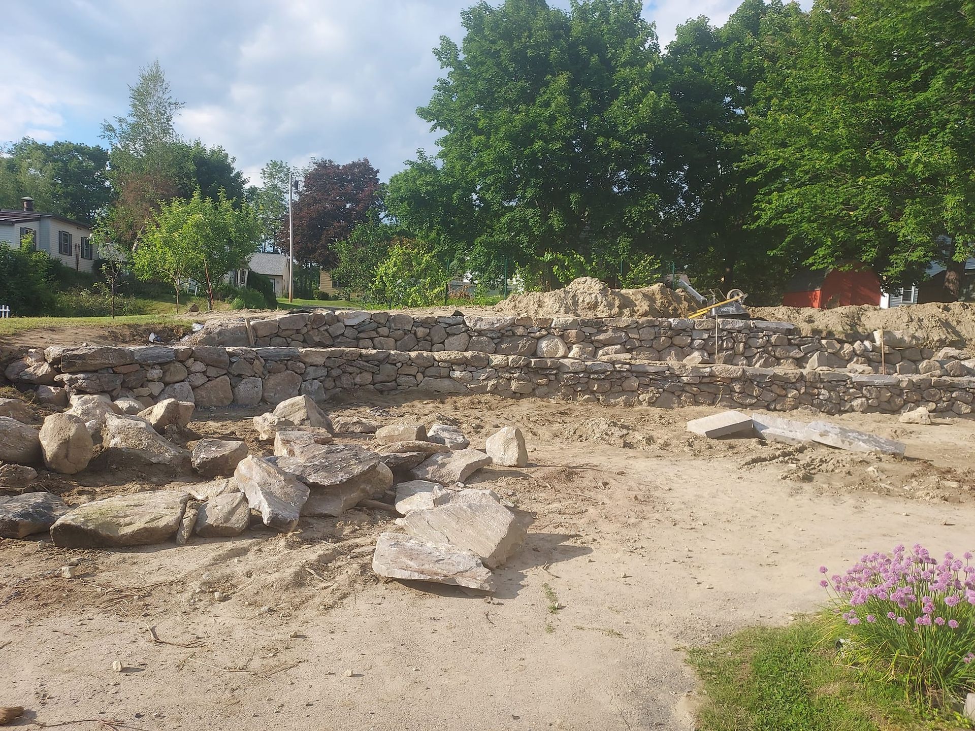 Debris-filled construction site; stone blocks, dirt, and low retaining walls with trees in the background.