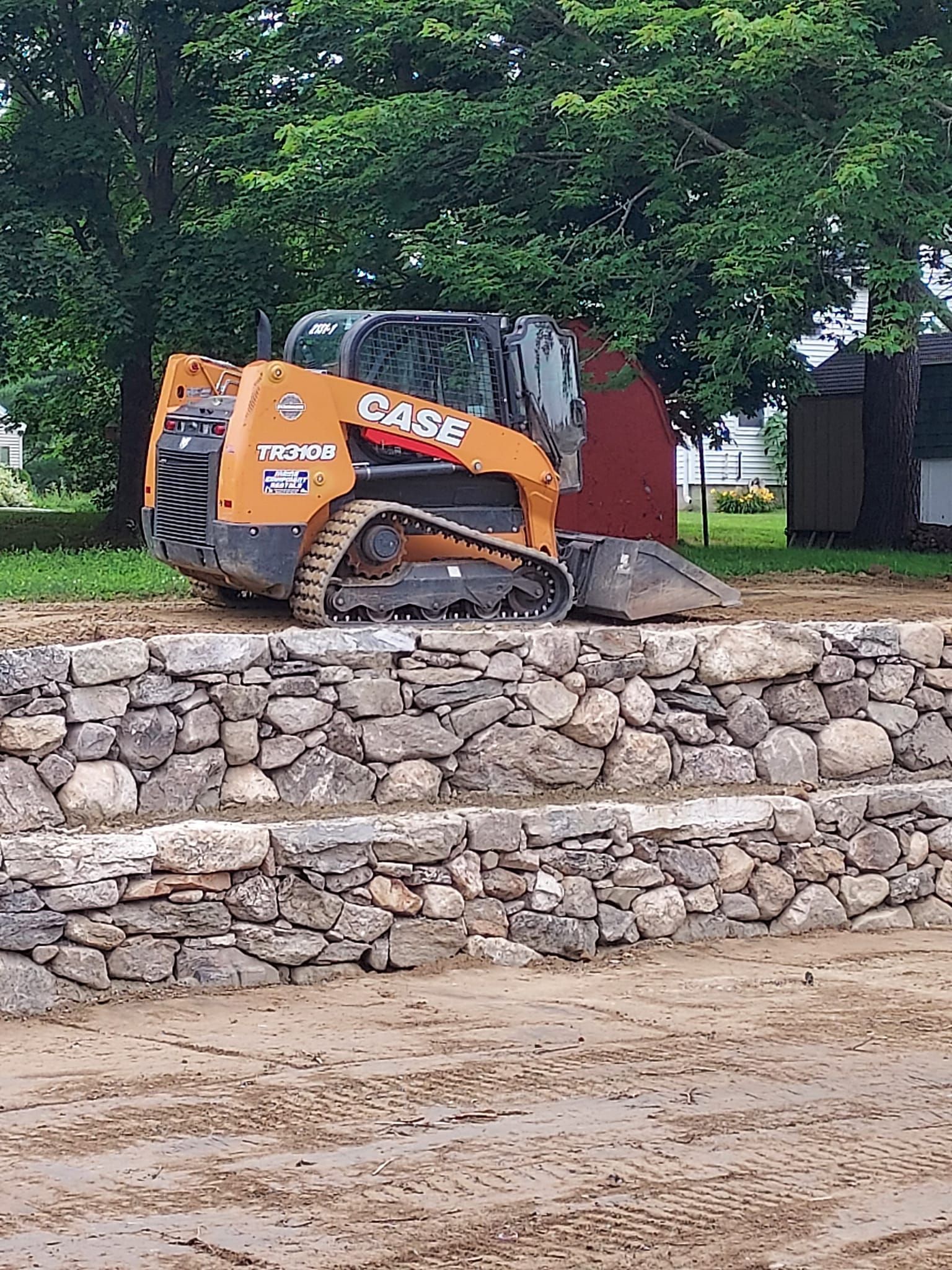 Orange Case skid steer loader on stone wall, operating in a muddy outdoor setting.