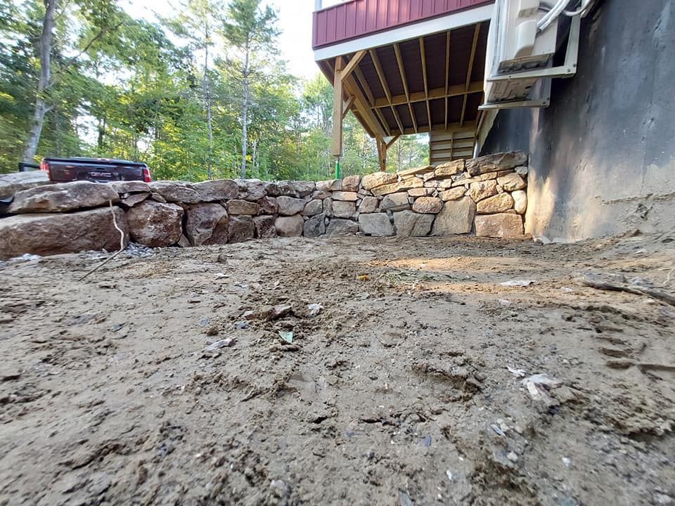 A stone retaining wall beneath a red-sided deck; muddy ground in front.
