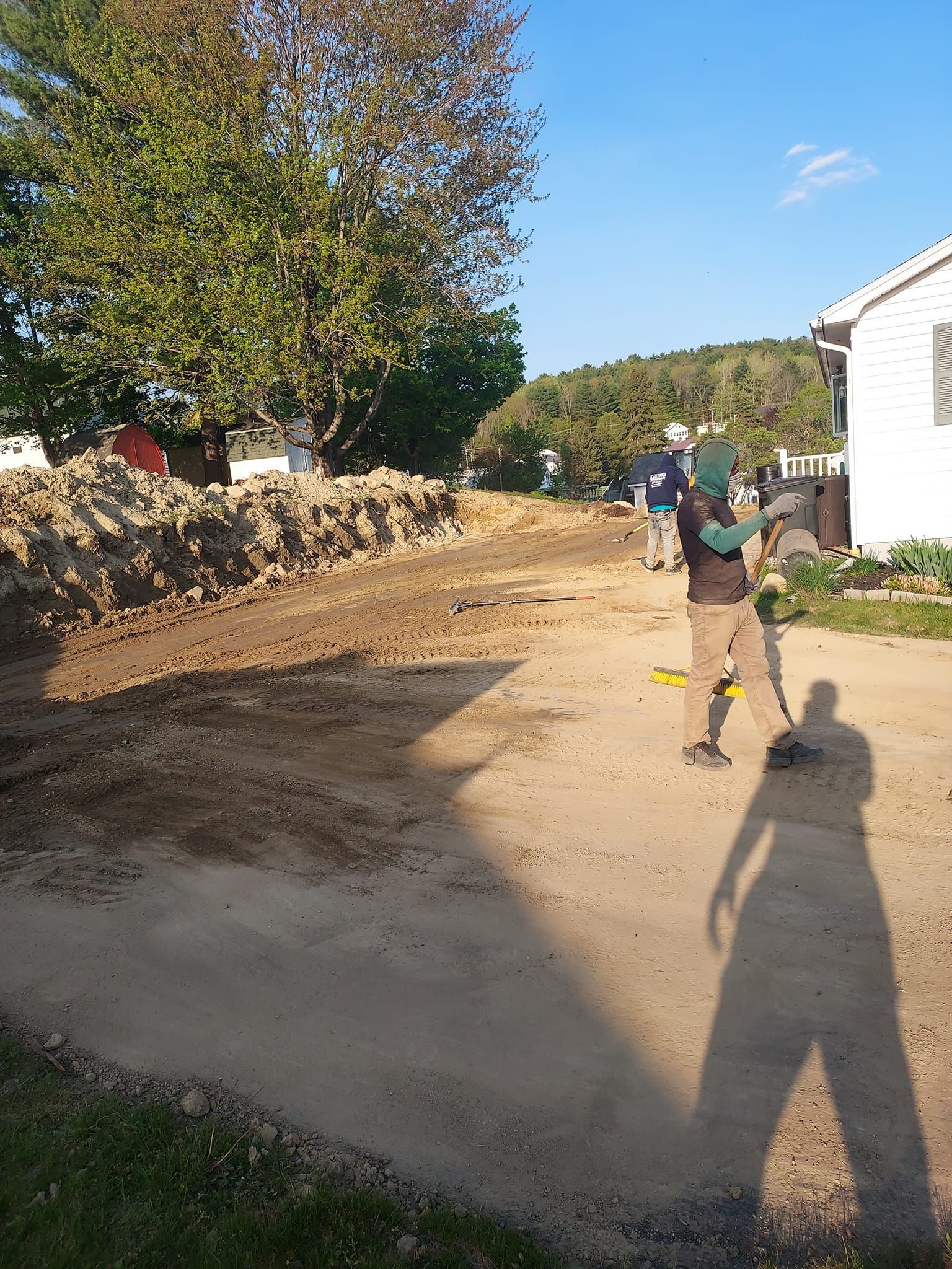 Person with a costume surveying a dirt road next to a house and a large pile of dirt.