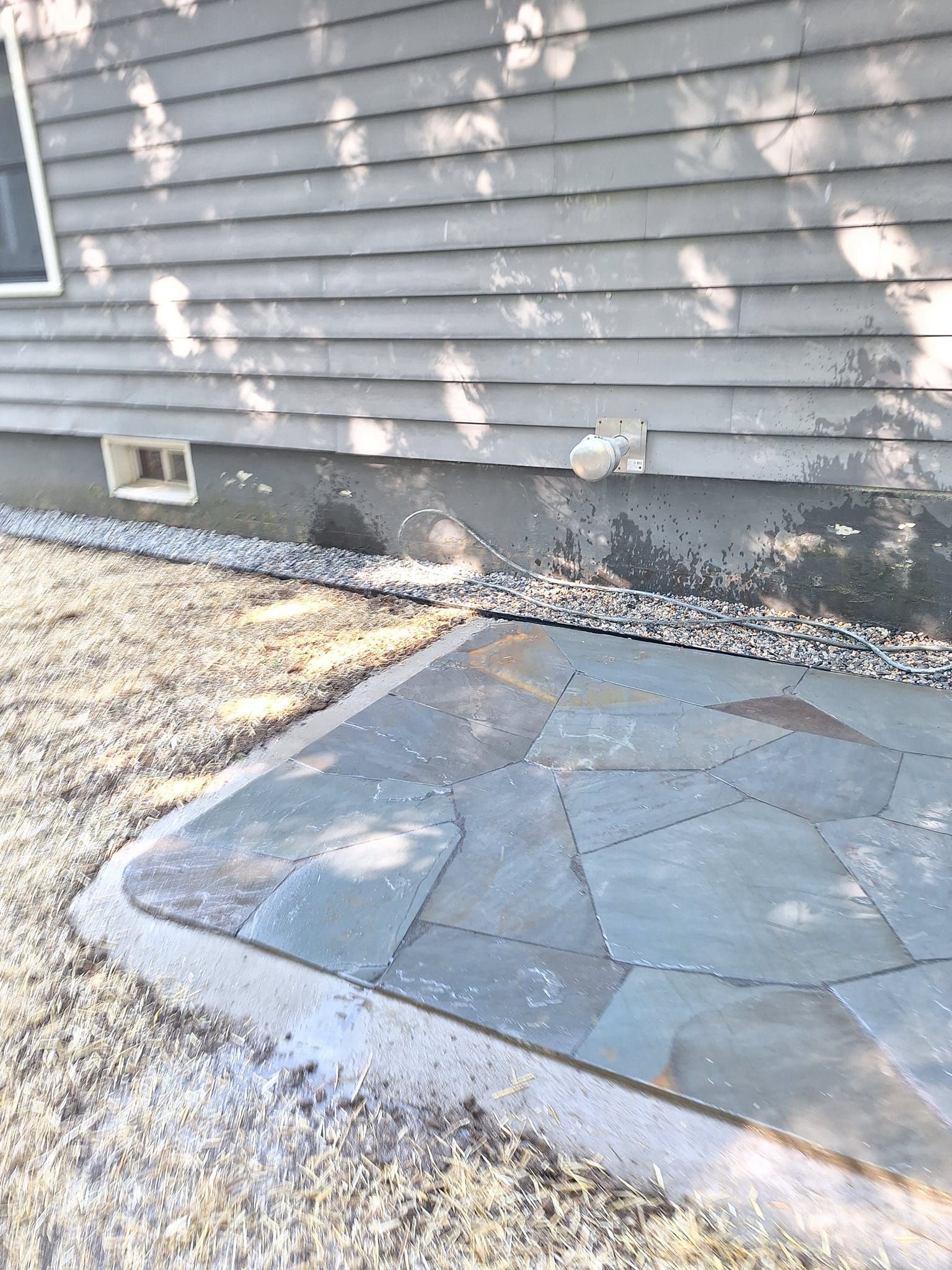 Exterior of a house with a stone patio, gravel, and gray siding.