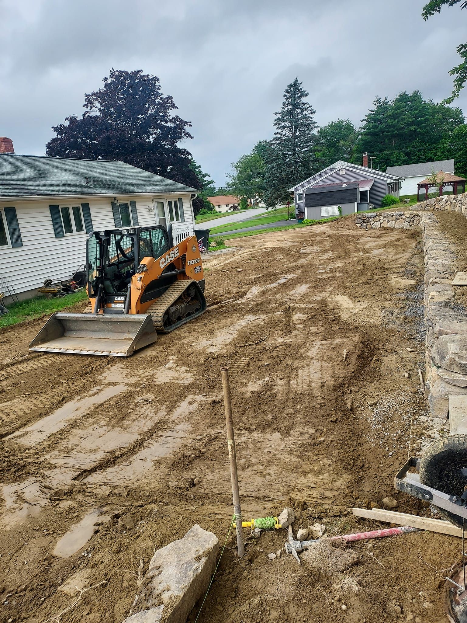 A small bulldozer on a muddy, excavated lot next to a house.