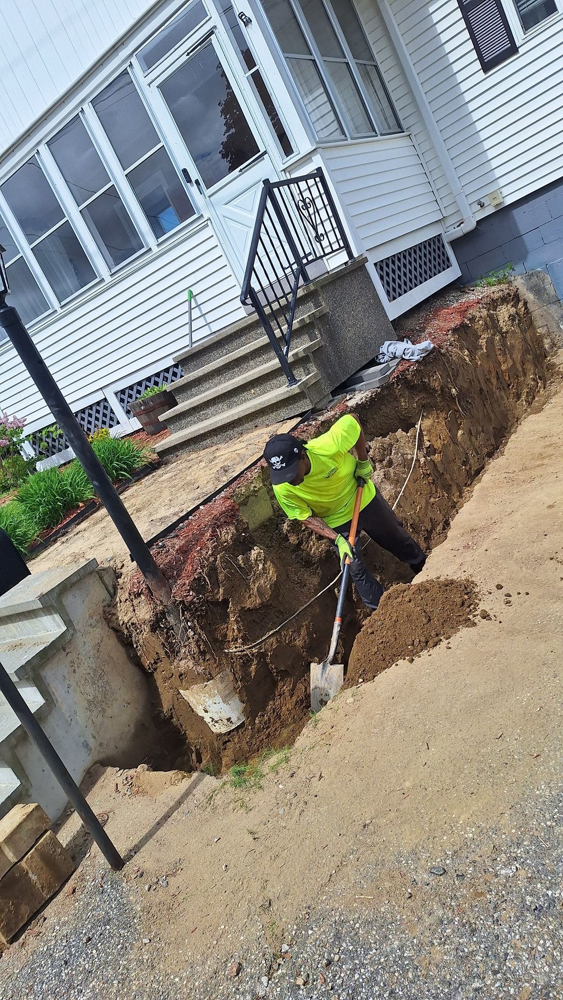 Person in high-vis jacket digging a trench near a house.
