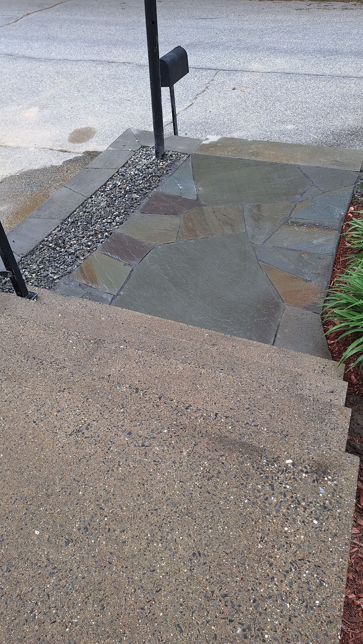 Stone steps leading up to a landing with a mailbox and dark stones.