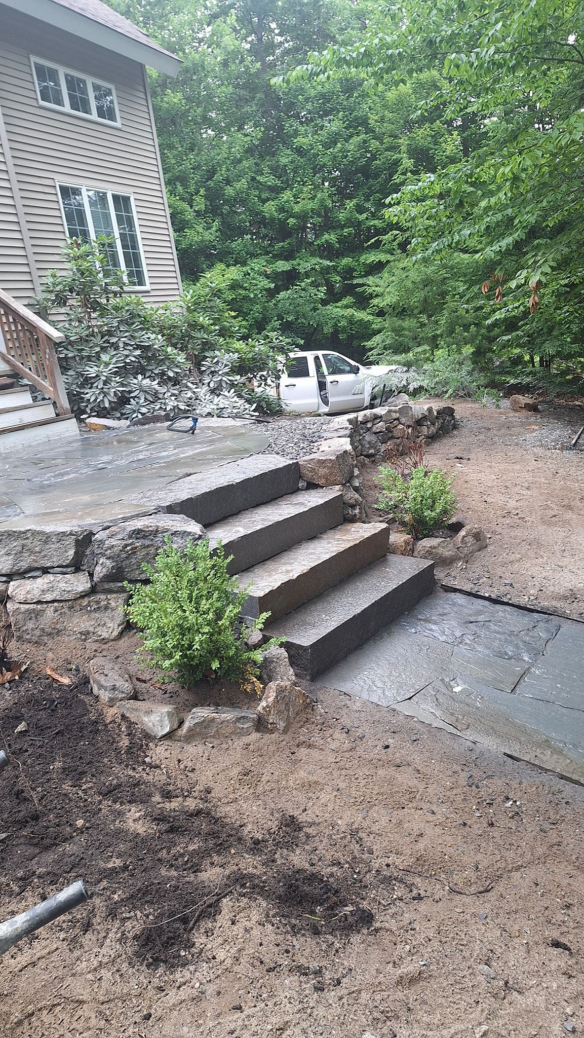 Stone steps leading up to a house with surrounding landscaping and a parked vehicle.