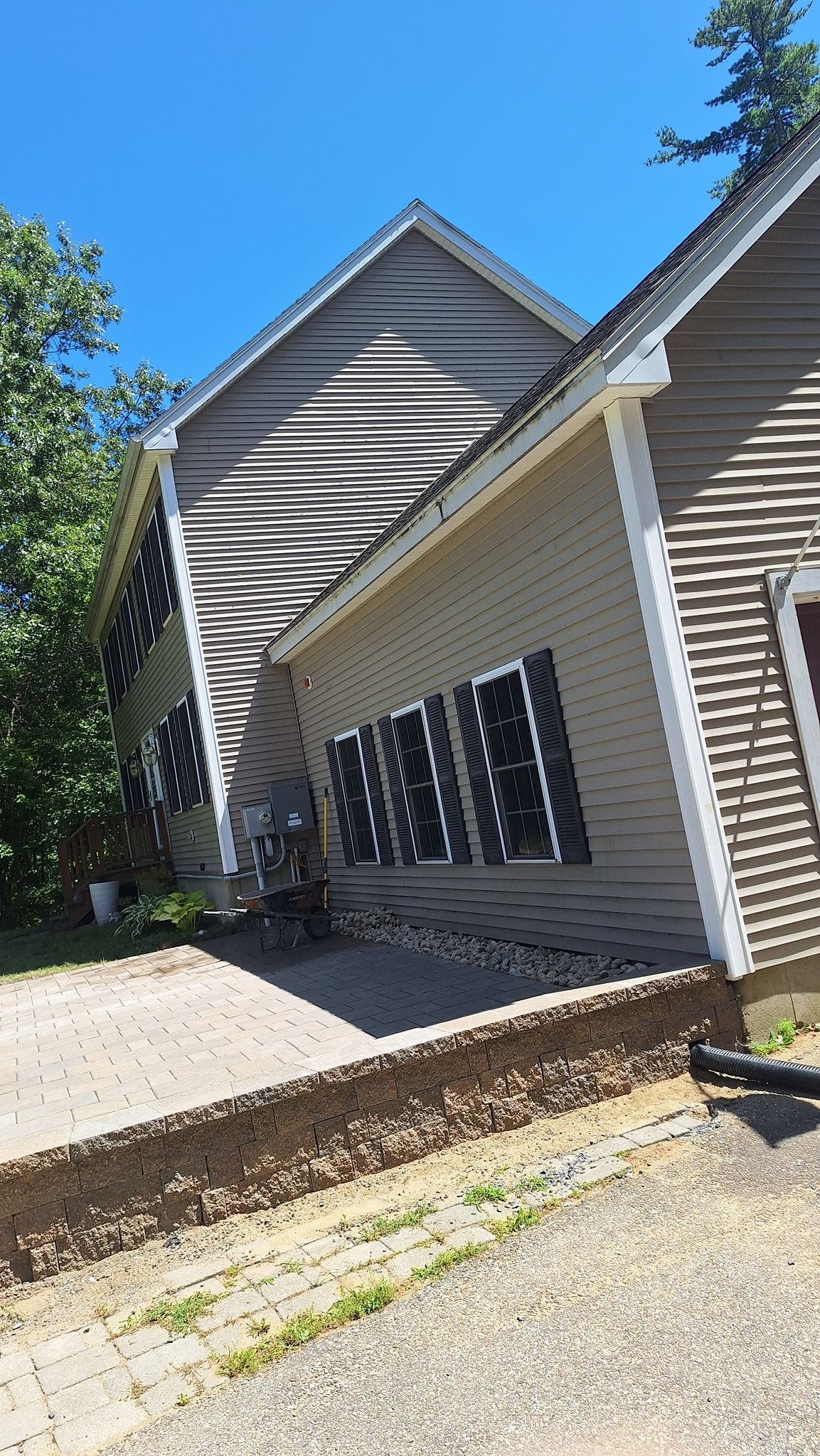A light brown house with a grey roof. Black shutters on windows. A sunny, outdoor scene.