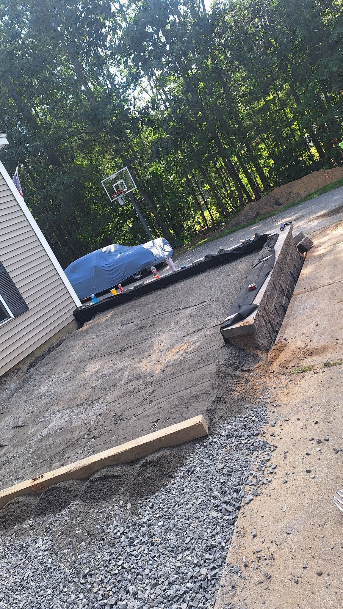 Gravel driveway with wooden borders, leading up to a white building, trees in background.