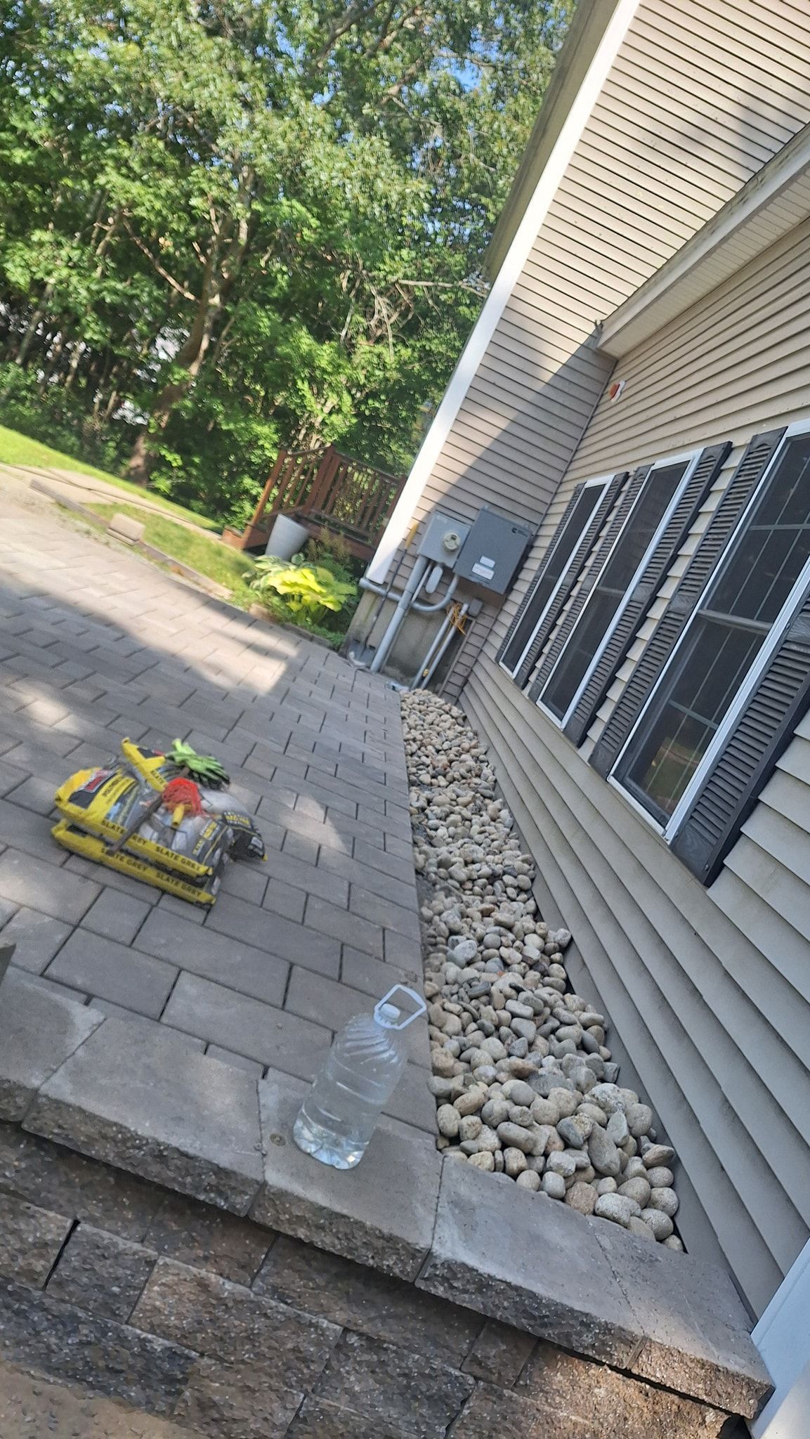 A paved patio with landscaping rocks and a building with shutters. A tool box and water bottle are on the patio.