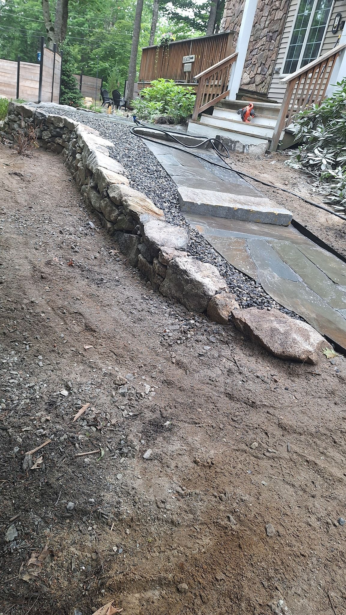 Sloped gravel pathway with stone border leading uphill toward a house.