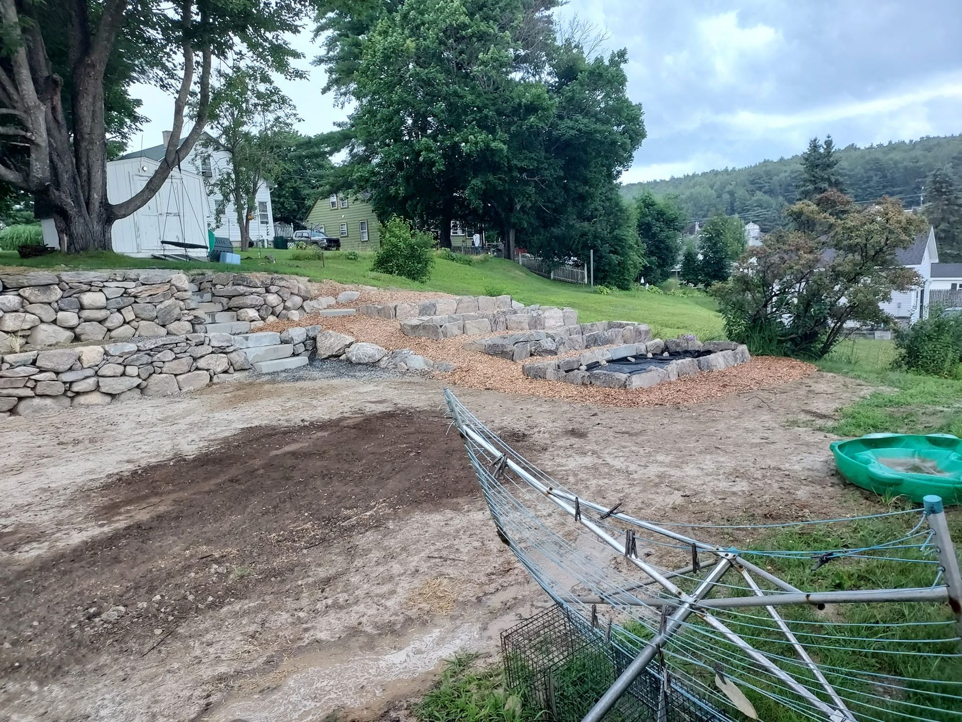 A hillside with stone walls and exposed brick foundations. A clothes drying rack sits in the foreground.